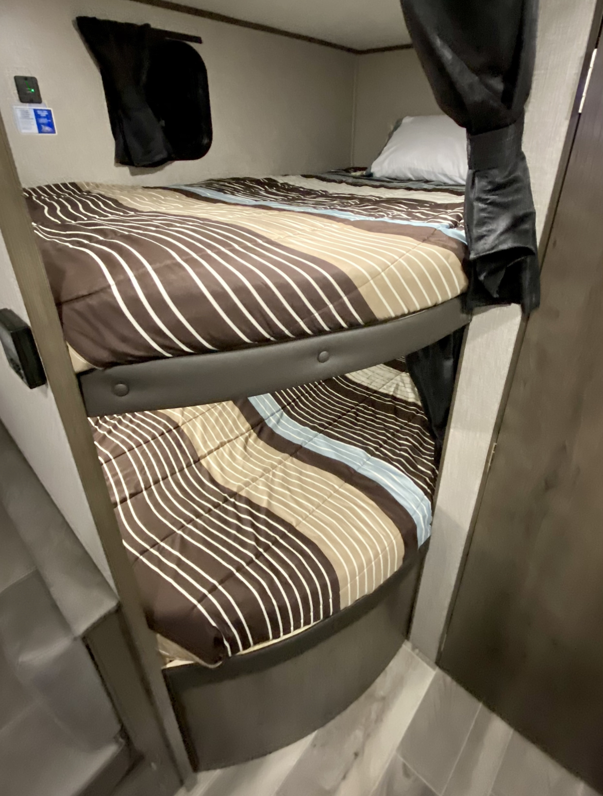Cozy RV rental bunk beds, adorned with striped brown, tan, and white bedding, offer comfortable sleeping for travel. Black curtains visible.. Jayco Jay Flight SLX 2021