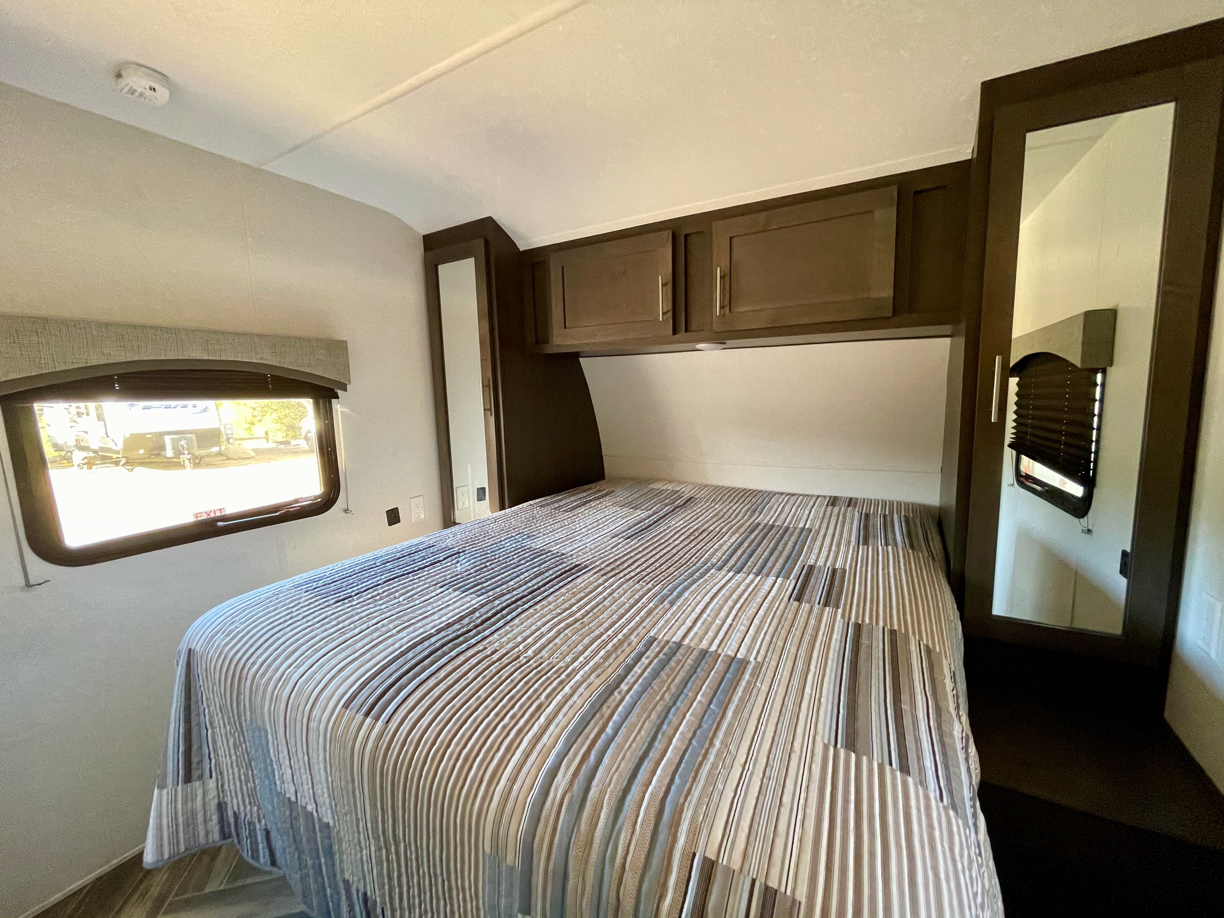 Inside an RV rental: a cozy bedroom with a striped bed, overhead storage, and a window for scenic views.. Forest River Evo 2850 2019