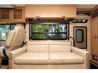 Comfortable RV rental living area with a sofa, overhead cabinets, and large window, perfect for your travel adventures.. Thor A.C.E. 2018