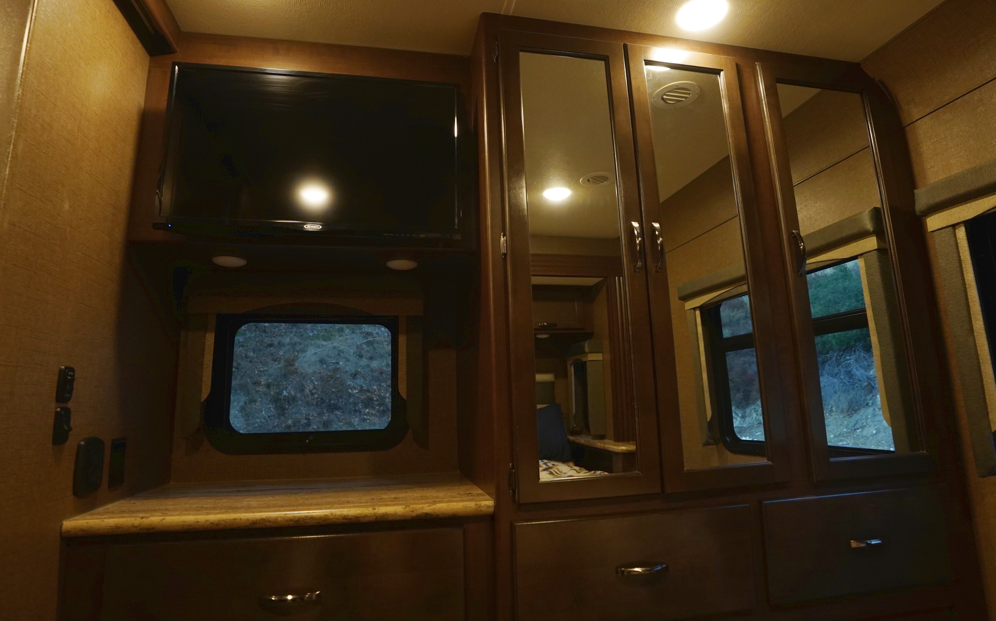 RV rental interior: bedroom features like a TV, mirrored storage, and windows showing an outdoor scene.. Thor Motor Coach A.C.E 2020