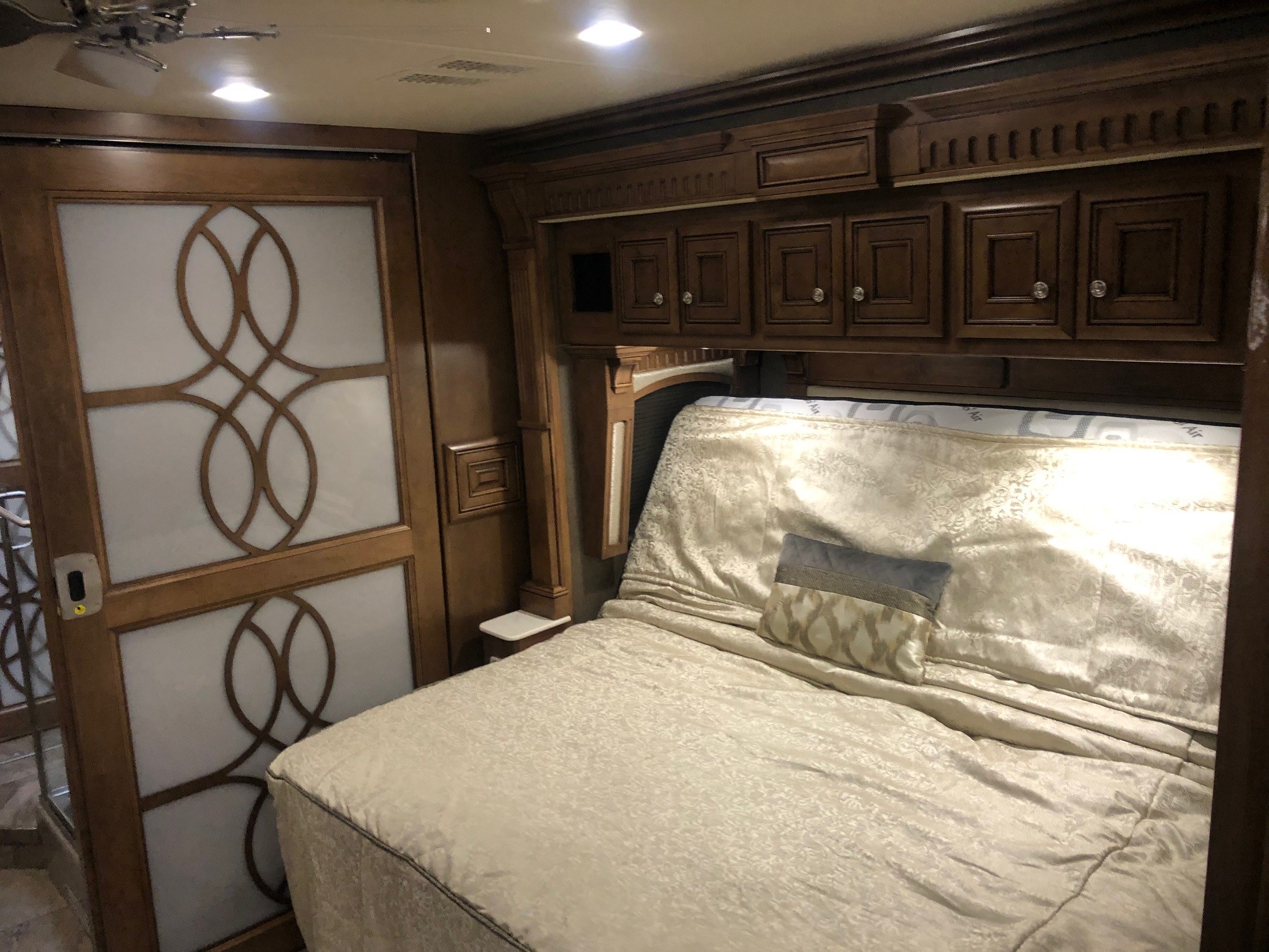 Spacious RV rental sleeping area with intricate wooden cabinetry, plush bedding, and decorative frosted door.. Monaco Signature 2020