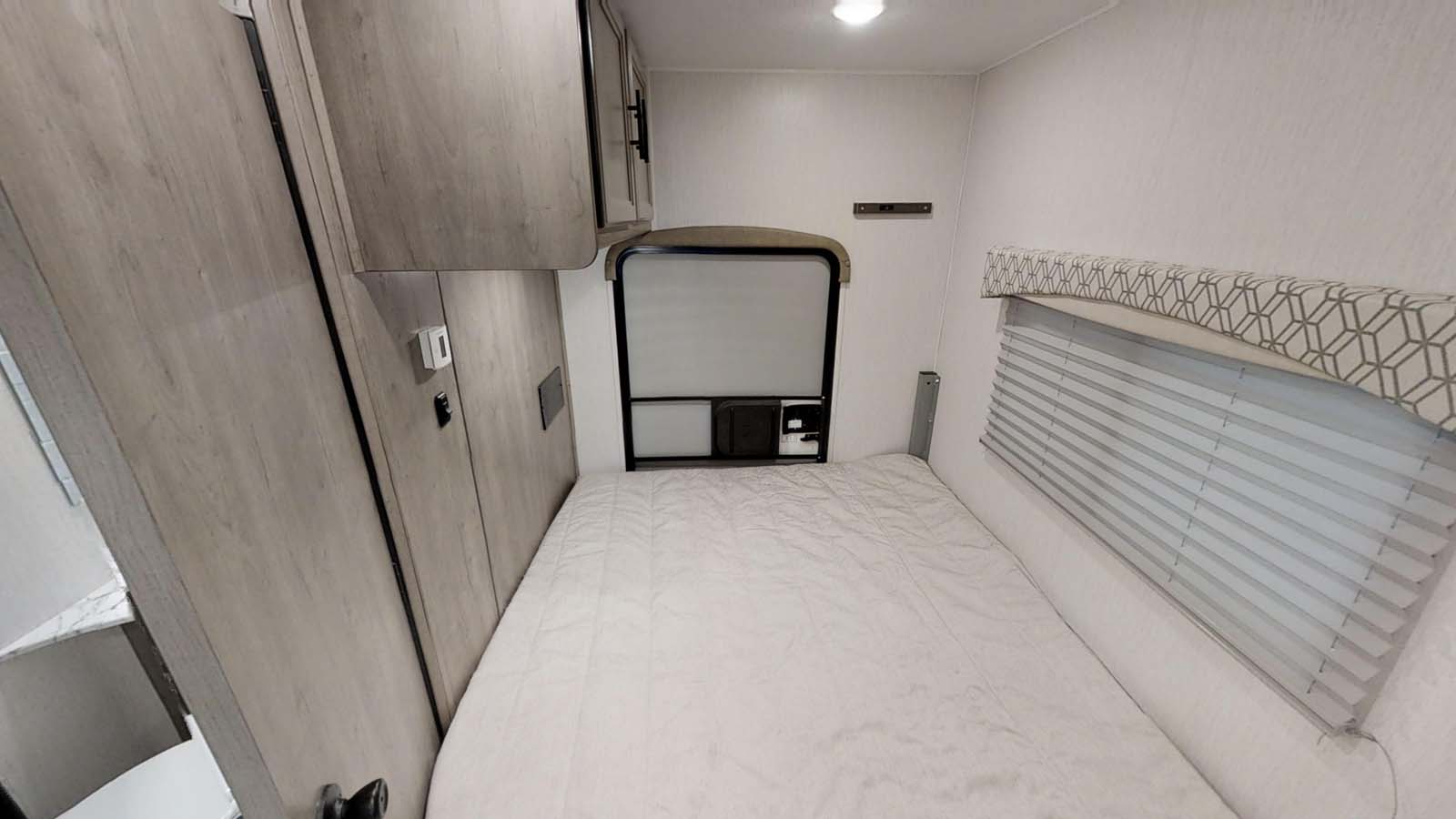 This RV rental bedroom features a comfy bed, wood-look cabinets, and a window with blinds.. Coachmen Freelander 2021