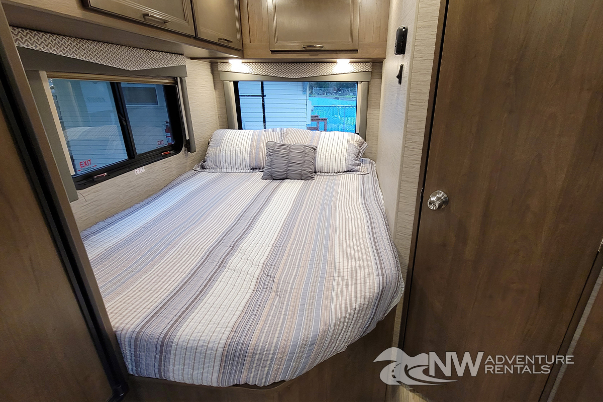 Cozy RV rental bedroom featuring a bed with striped bedding and windows. Perfect for travel adventures.. Thor Motor Coach Four Winds 2021