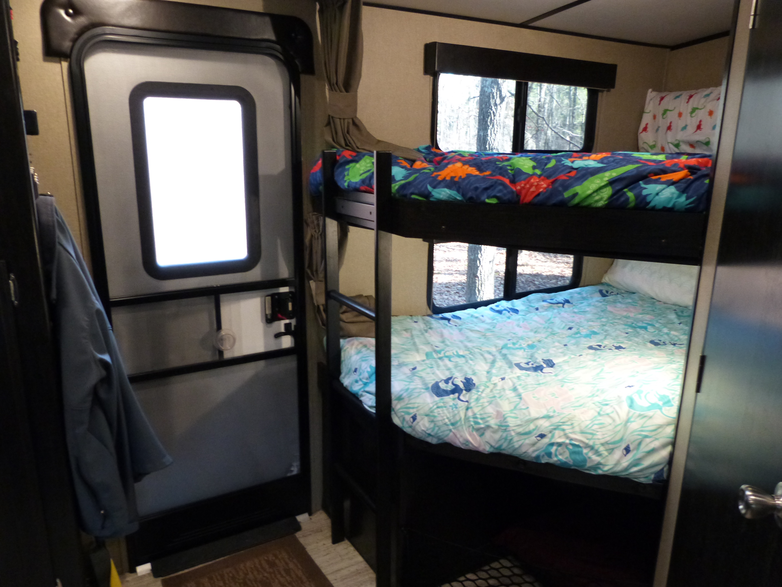 Cozy RV rental interior featuring bunk beds with colorful sheets and a view of trees outside, next to an entry door.. Grand Design 2400BH 2017