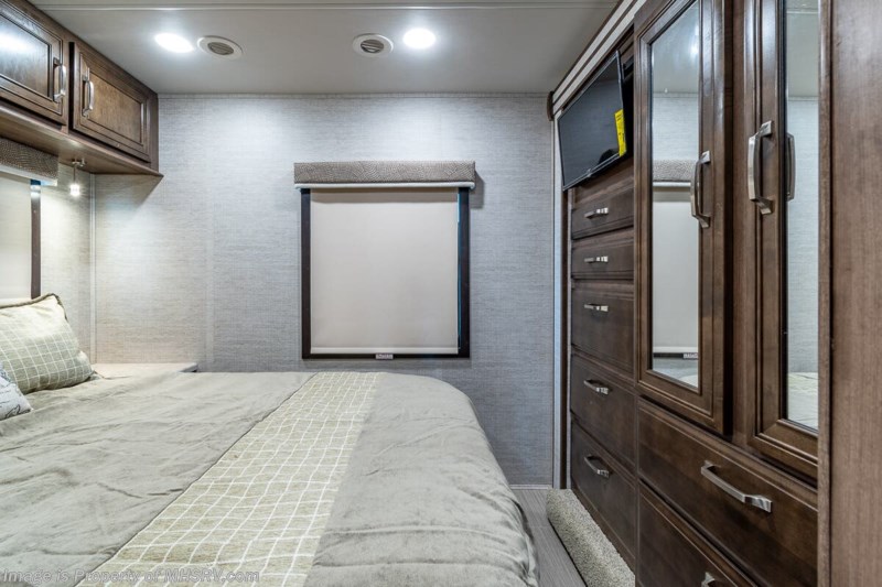 Cozy RV rental bedroom featuring a comfy bed, wall-mounted TV, wood cabinetry, and modern compact storage for travel.. Entegra Coach Other 2021