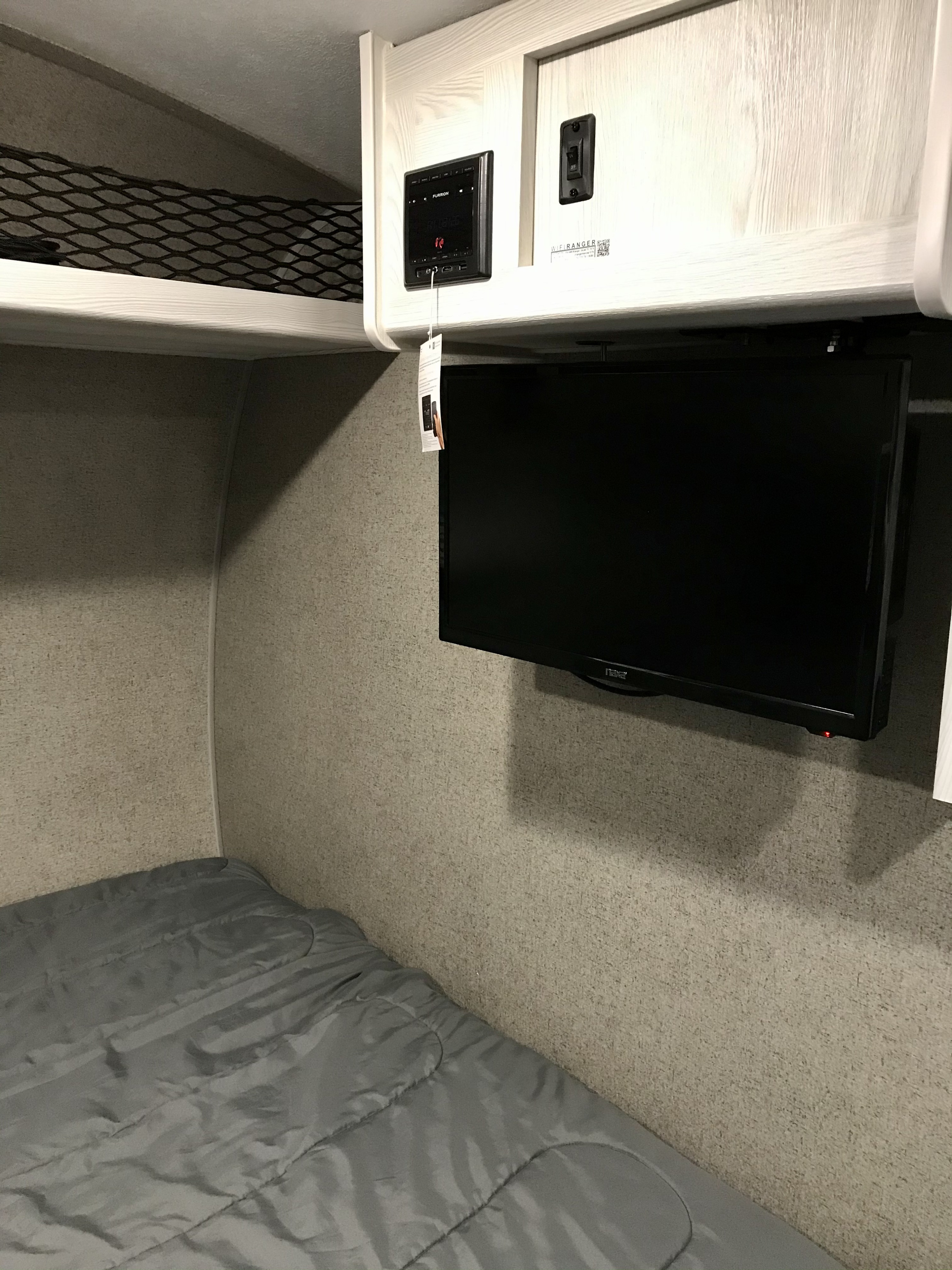 Cozy RV rental bedroom featuring a bed, wall-mounted TV, Furrion entertainment system, and handy overhead storage netting.. Other Other 2021