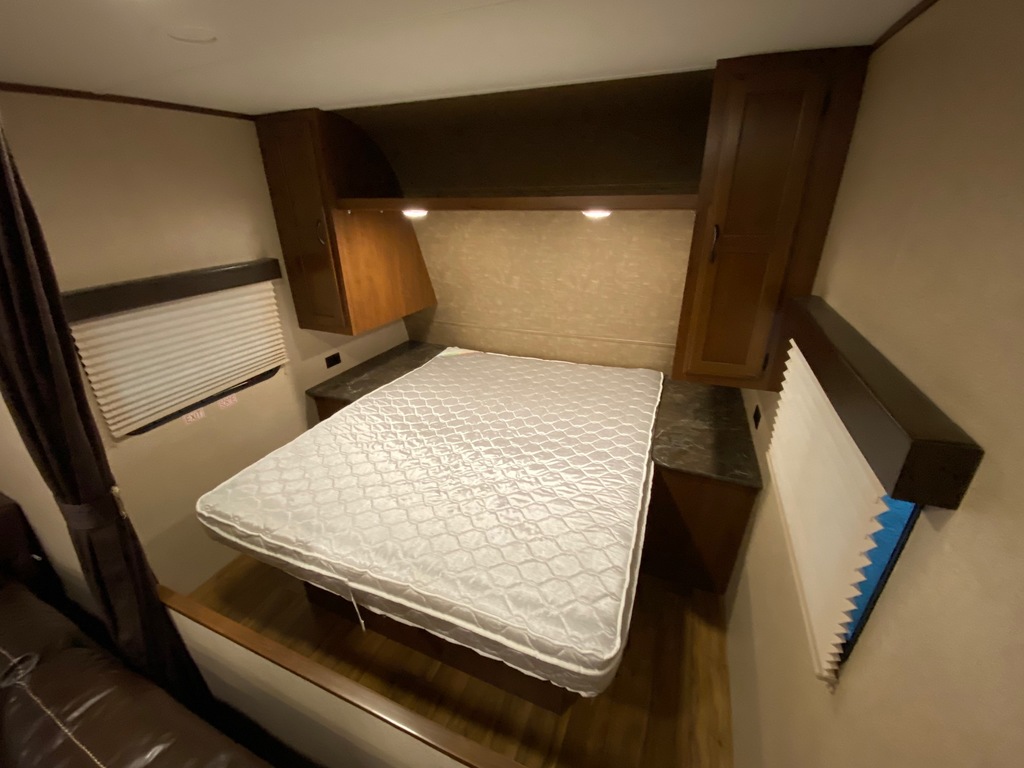 RV rental bedroom interior: a clean bed, overhead cabinets, and windows with blinds offer comfort on the road.. Jayco Jay Flight 2016