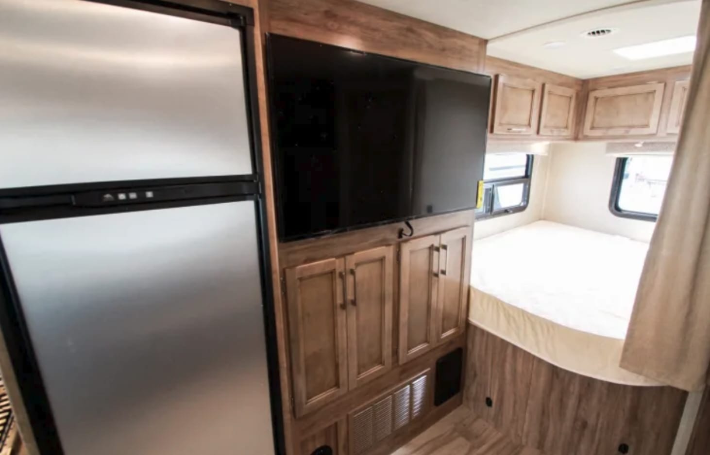 RV rental bedroom: Features include a fridge, wall-mounted TV, ample storage cabinets, and a bed with windows.. Entegra Coach Odyssey 25R 2019