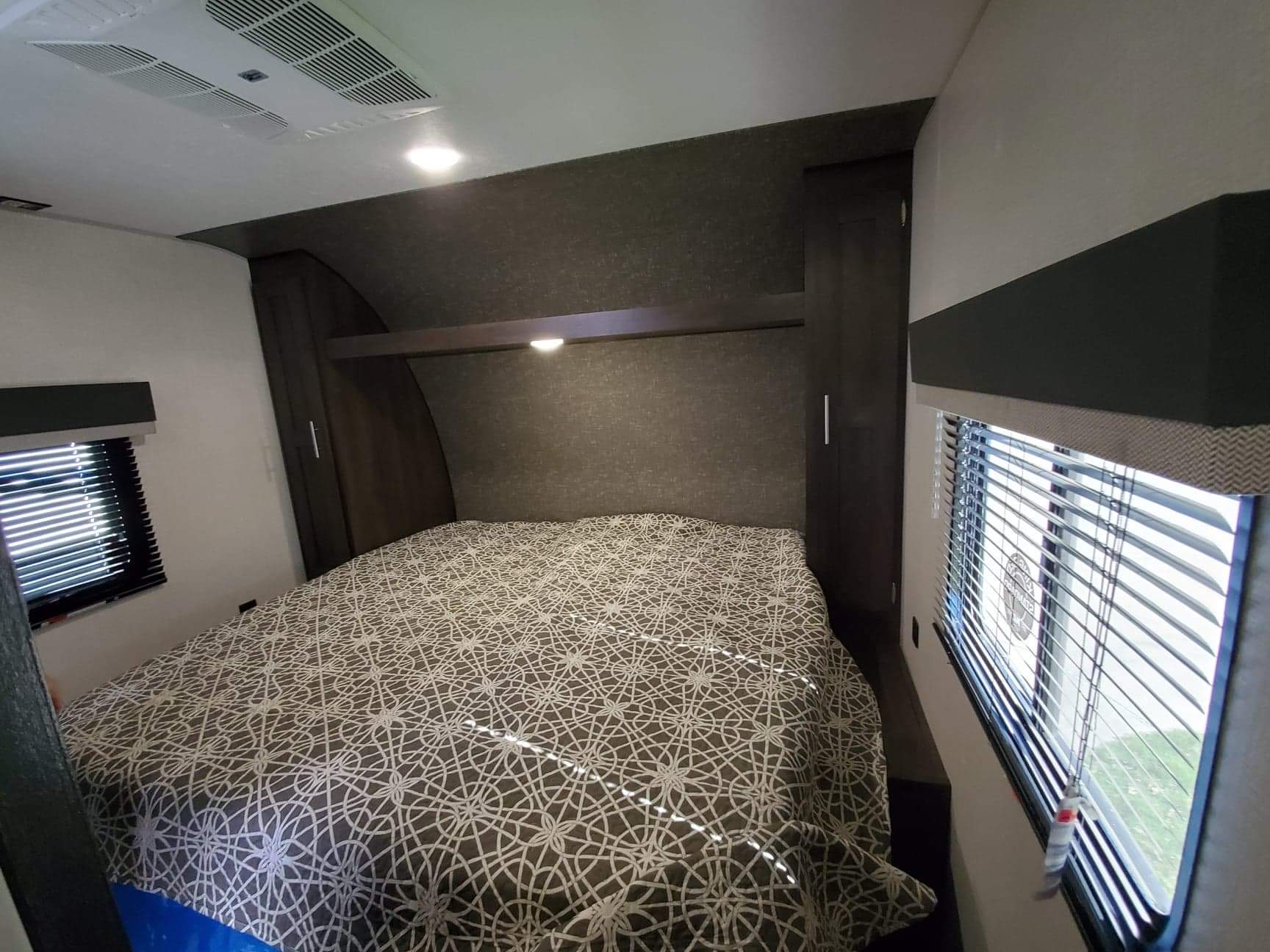 Comfortable RV rental bedroom with patterned bed, side windows & blinds, built-in wardrobes, and ceiling AC unit.. K-Z Manufacturing Sportsmen 2021