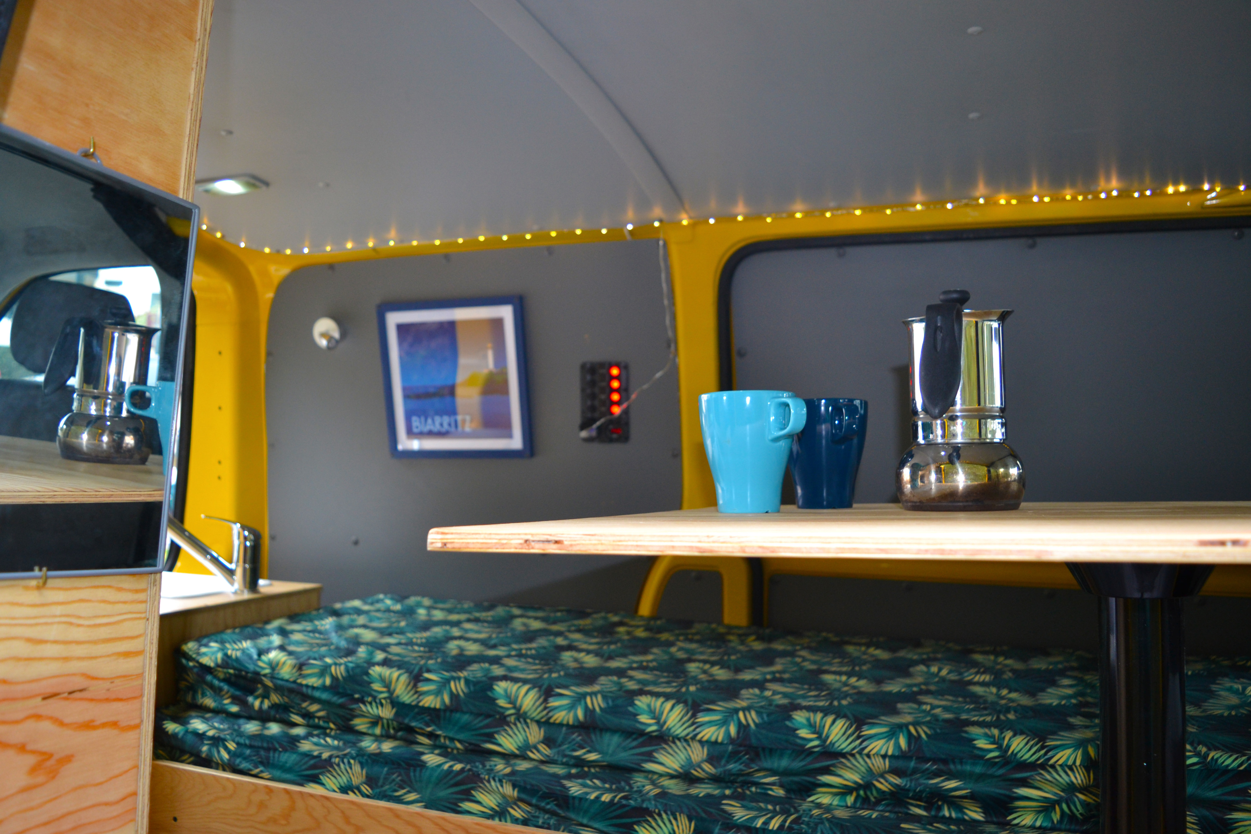 Cozy RV rental: yellow & grey interior with a compact kitchen, moka pot, tropical bed, and warm string lights.. Volkswagen Transporter T5 2012