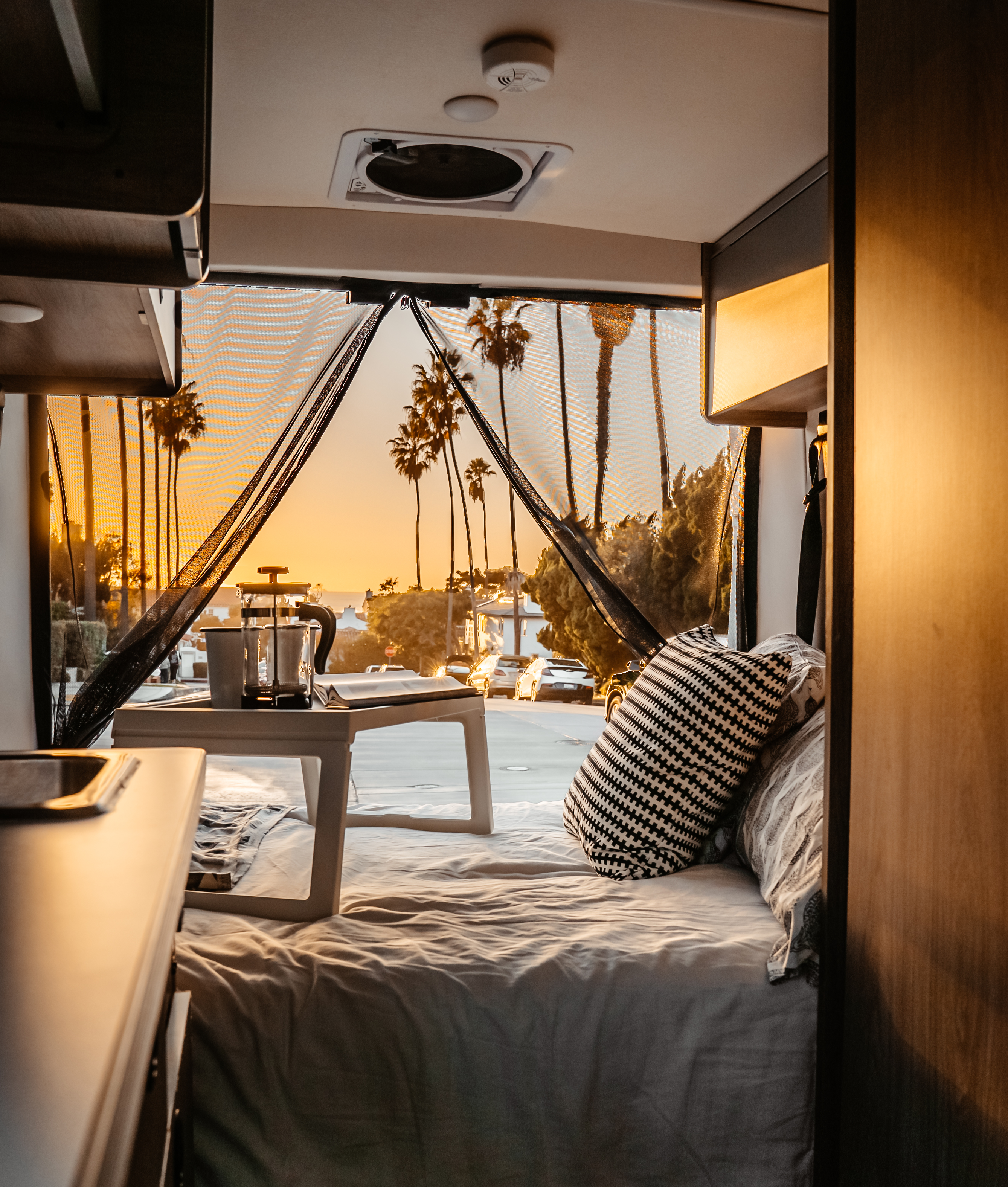 Cozy RV rental interior at sunset. Enjoy coffee & scenic palm tree views from your comfortable bed.. Winnebago Solis 2021