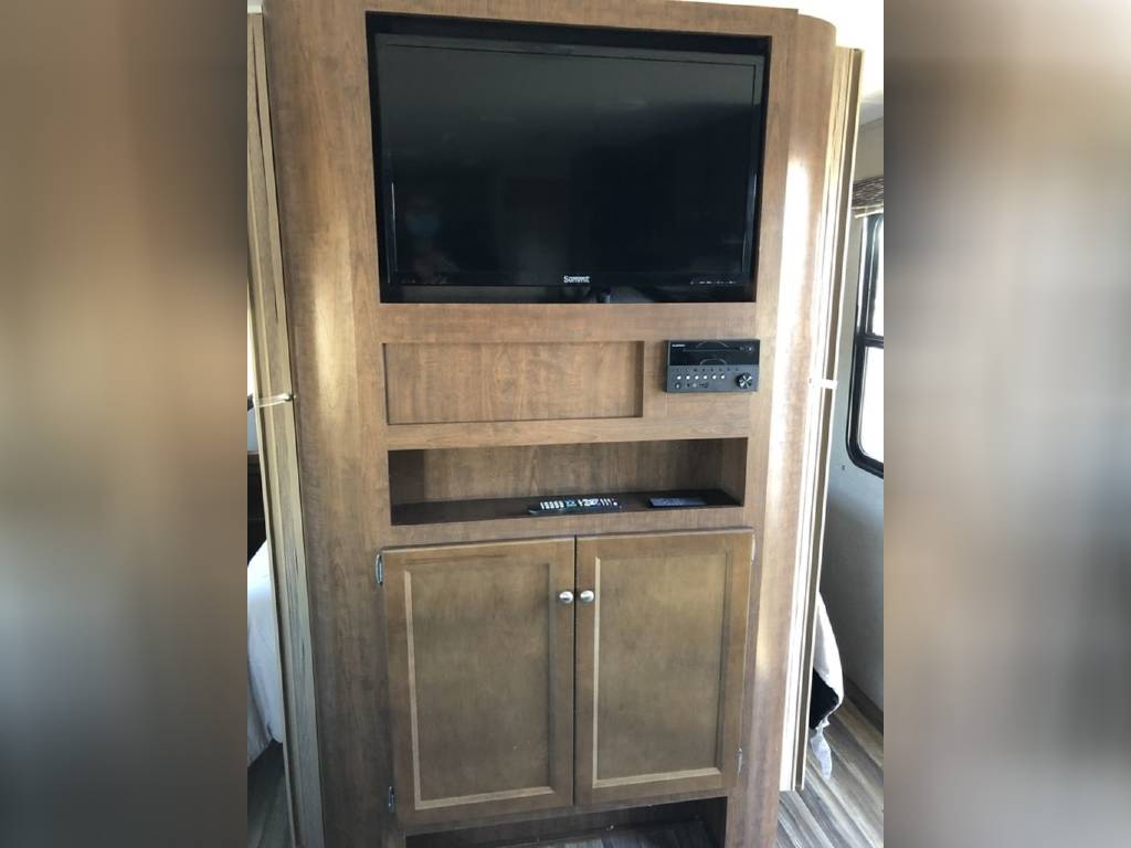 This RV rental interior features an entertainment center with a TV, audio system, and wood-look storage cabinets.. Keystone Hideout 2018