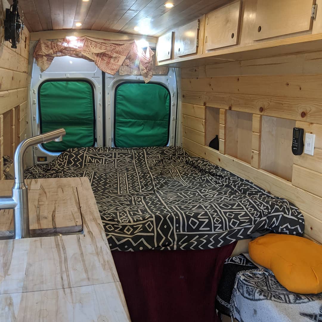 This RV rental's wood-paneled interior features a cozy bed, kitchen sink, and clever storage options for van life.. Ford Transit Custom 2019