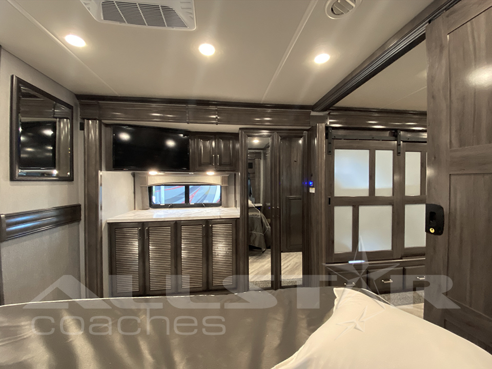 Spacious RV rental bedroom featuring a TV, cabinets, and sliding door for comfortable journeys.. Fleetwood Pace Arrow 2021