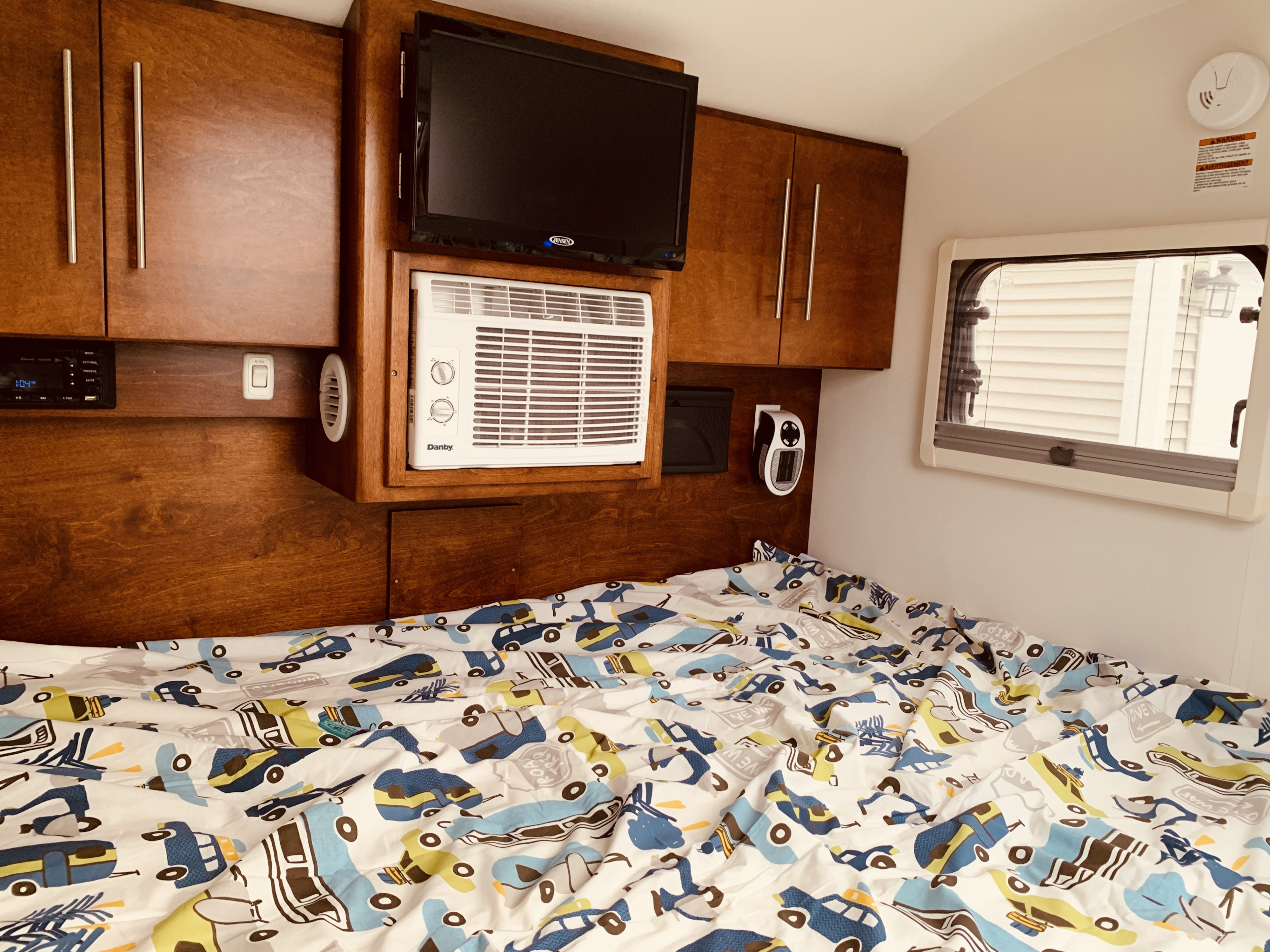 Cozy RV rental interior with a bed, TV, AC, and wooden cabinets. Playful car-themed bedding adds a fun touch.. American Teardrop Travel Trailer 2019