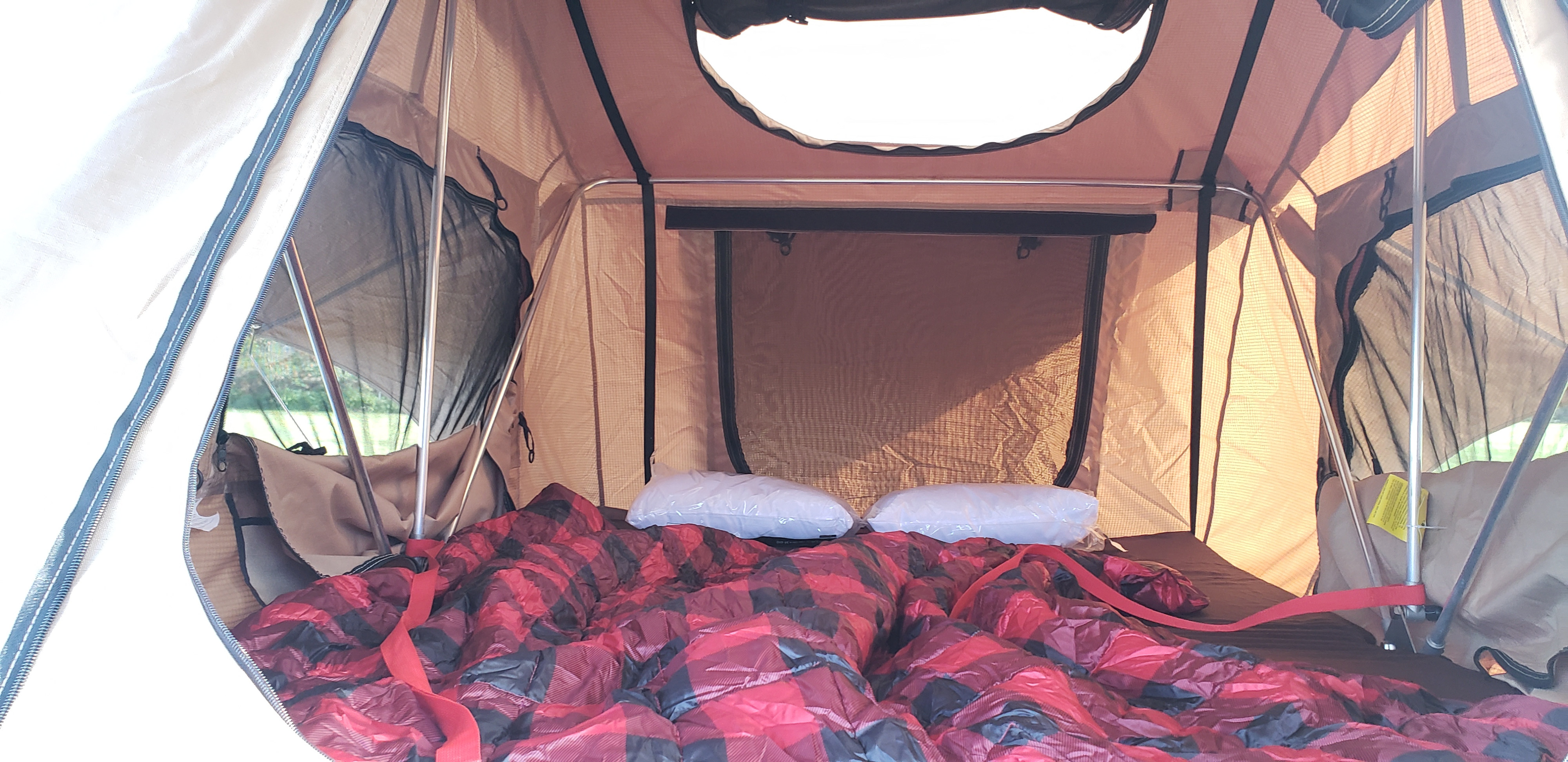 Cozy rooftop tent interior for RV rental adventures. Plaid blanket, pillows, and mesh windows offer comfort with an outdoor view.. Jeep wrangler unlimited 2017