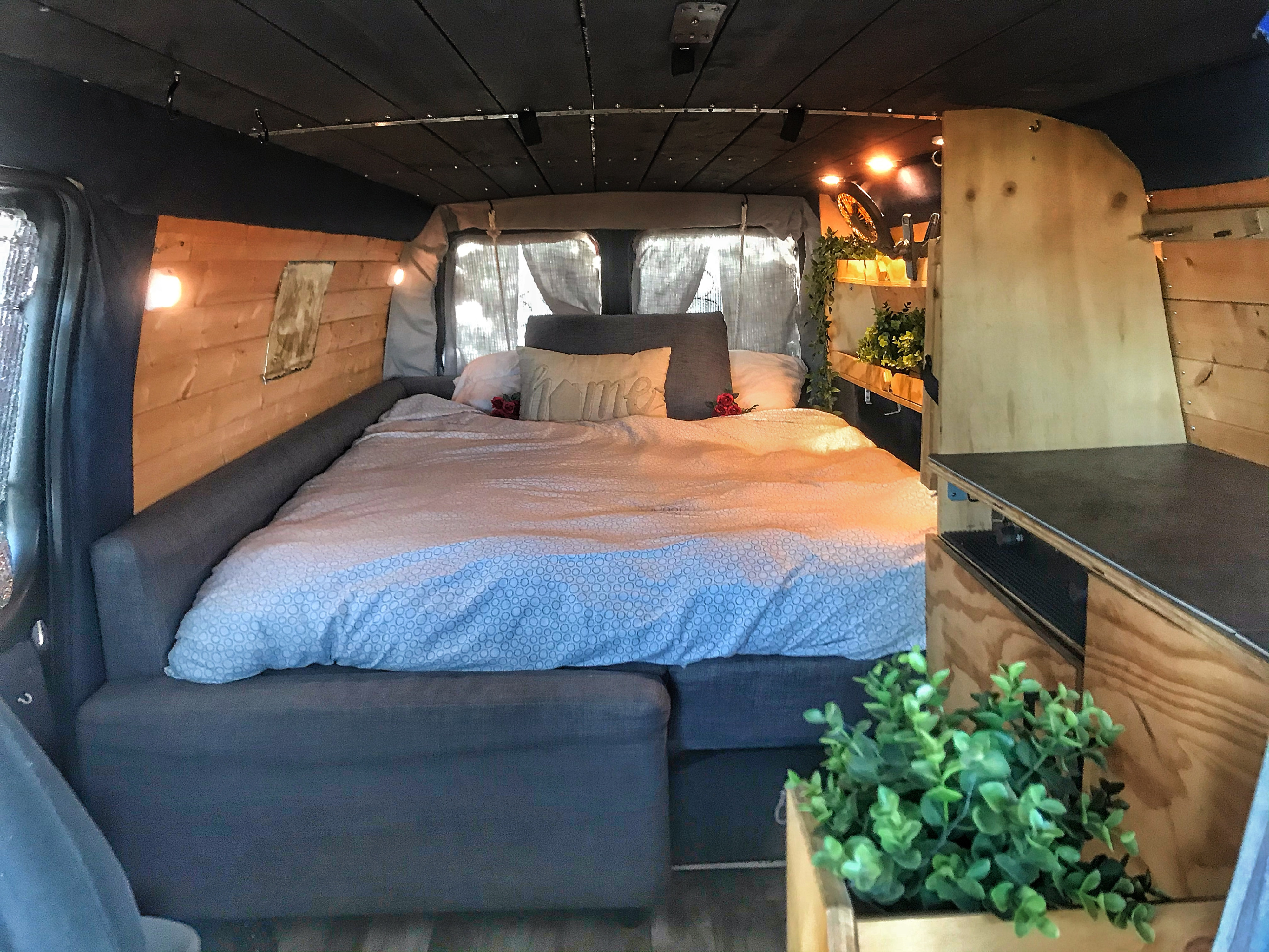 Cozy rv rental van interior with a large, comfy bed, wooden paneled walls, and warm ambient lighting. Ideal for travel.. Ford Econoline Extended 2006