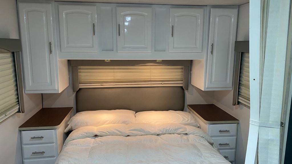 Cozy RV rental bedroom featuring bright white cabinets, comfy bed, and bedside storage for your journey.. Jayco Greyhawk 2002