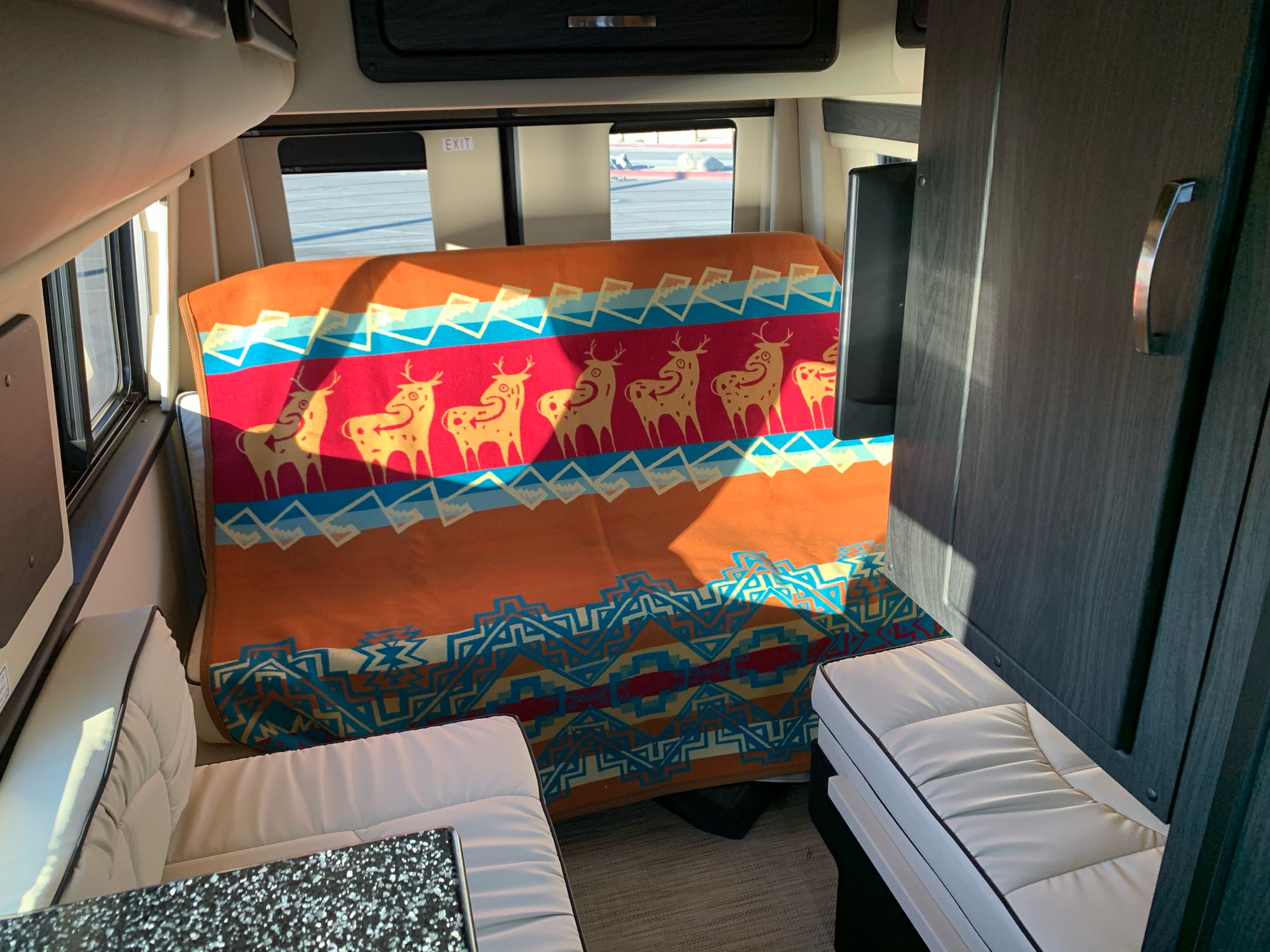 RV rental interior with a cozy bed covered by a vibrant deer-patterned blanket, light seating, and dark cabinetry.. Midwest Automotive Designs Midwest Automotive Designs Class B 2021