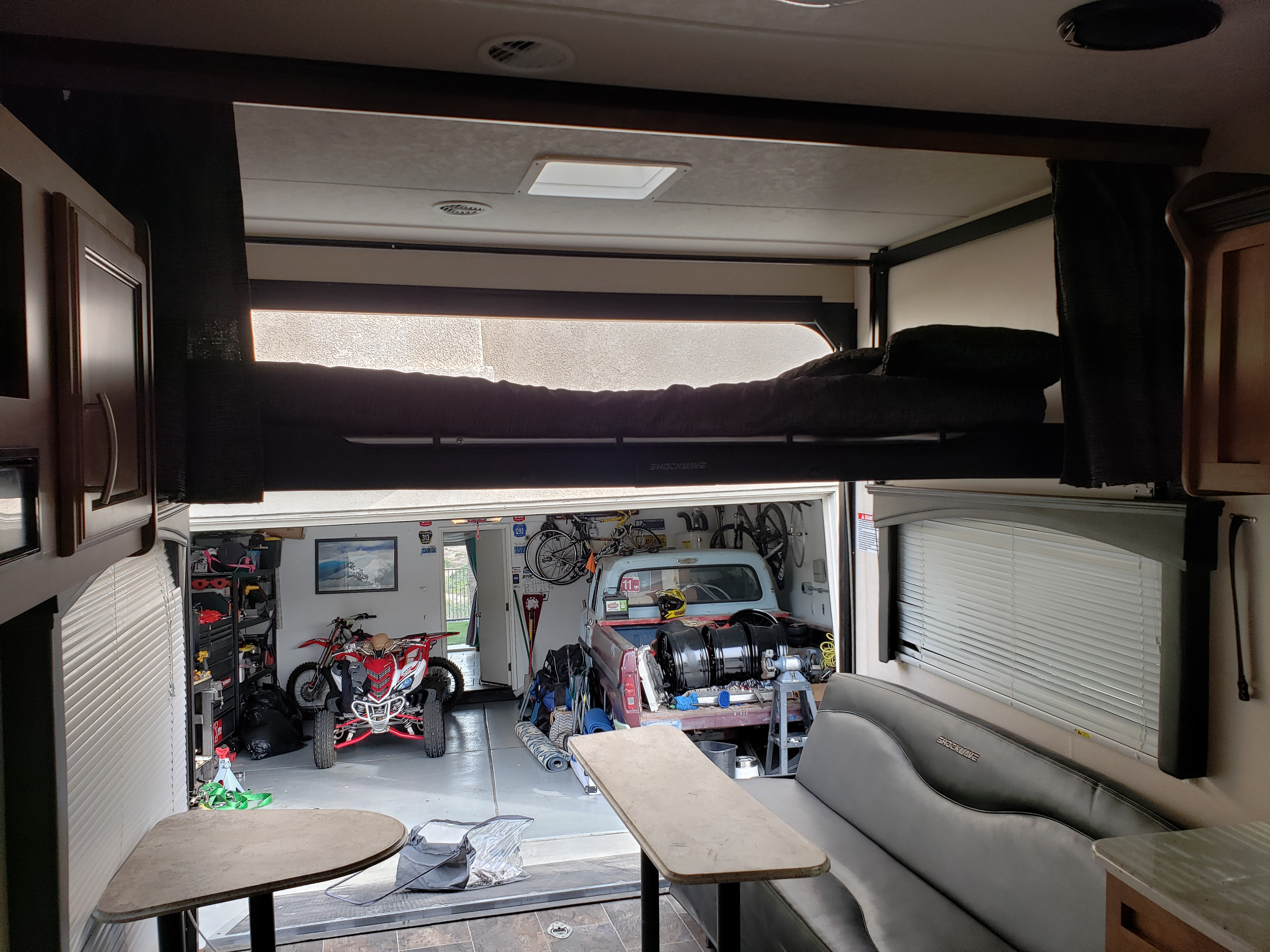 Inside an RV rental toy hauler, featuring a comfortable dinette, upper bunk beds, and a garage filled with an ATV, dirt bike, and pickup.. Forest River Shockwave 2017