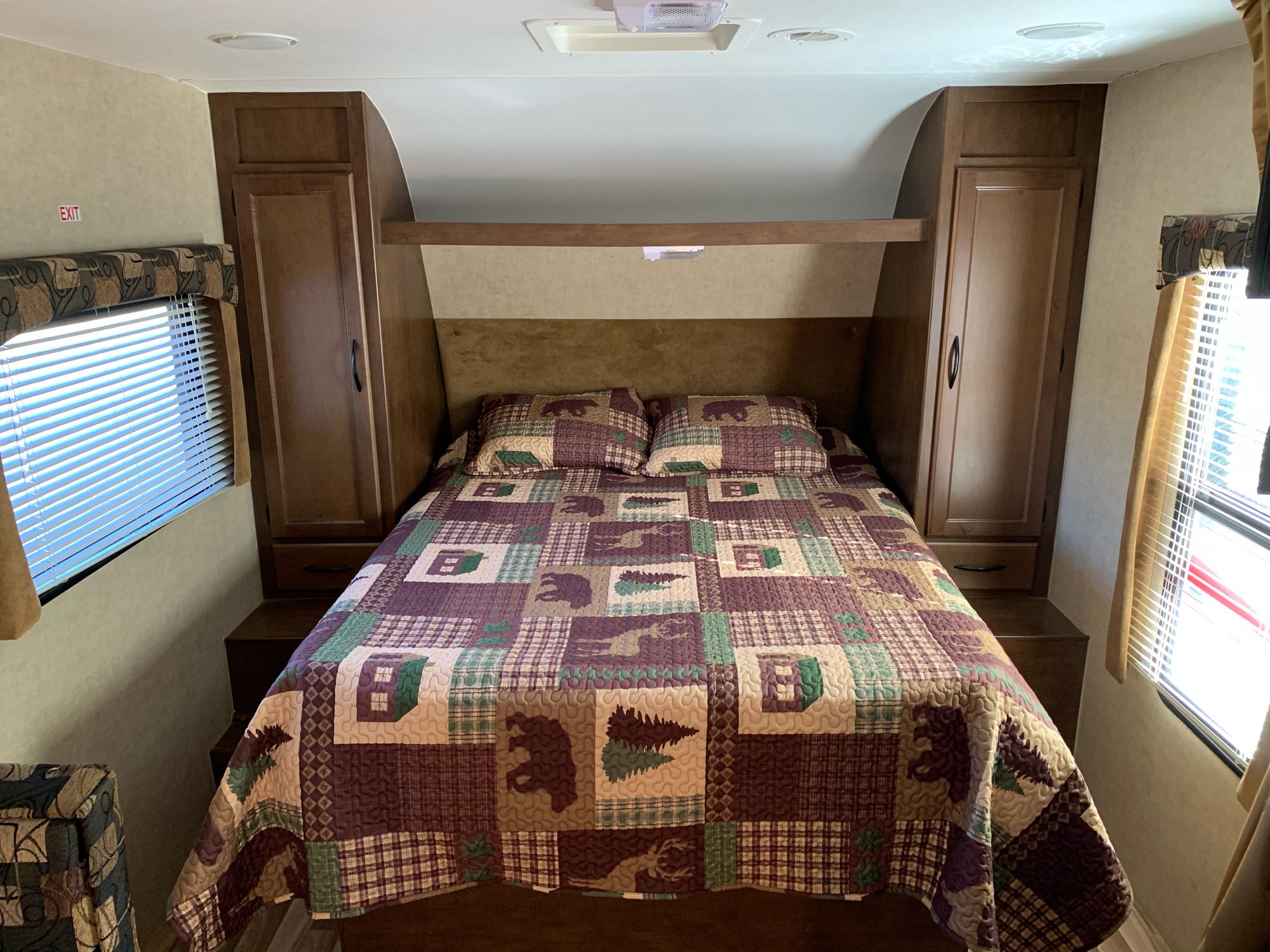 Inside an **RV rental**: a neat bedroom featuring a bed with a wilderness-themed quilt, side cabinets, and windows with blinds.. Pacific Coachworks Other 2016