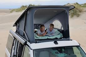Two boys enjoy a book in an RV rental pop-top campervan tent on a sandy beach, perfect for family camping adventures.. VW California T6 .1 2021 model Year Ocean 2021
