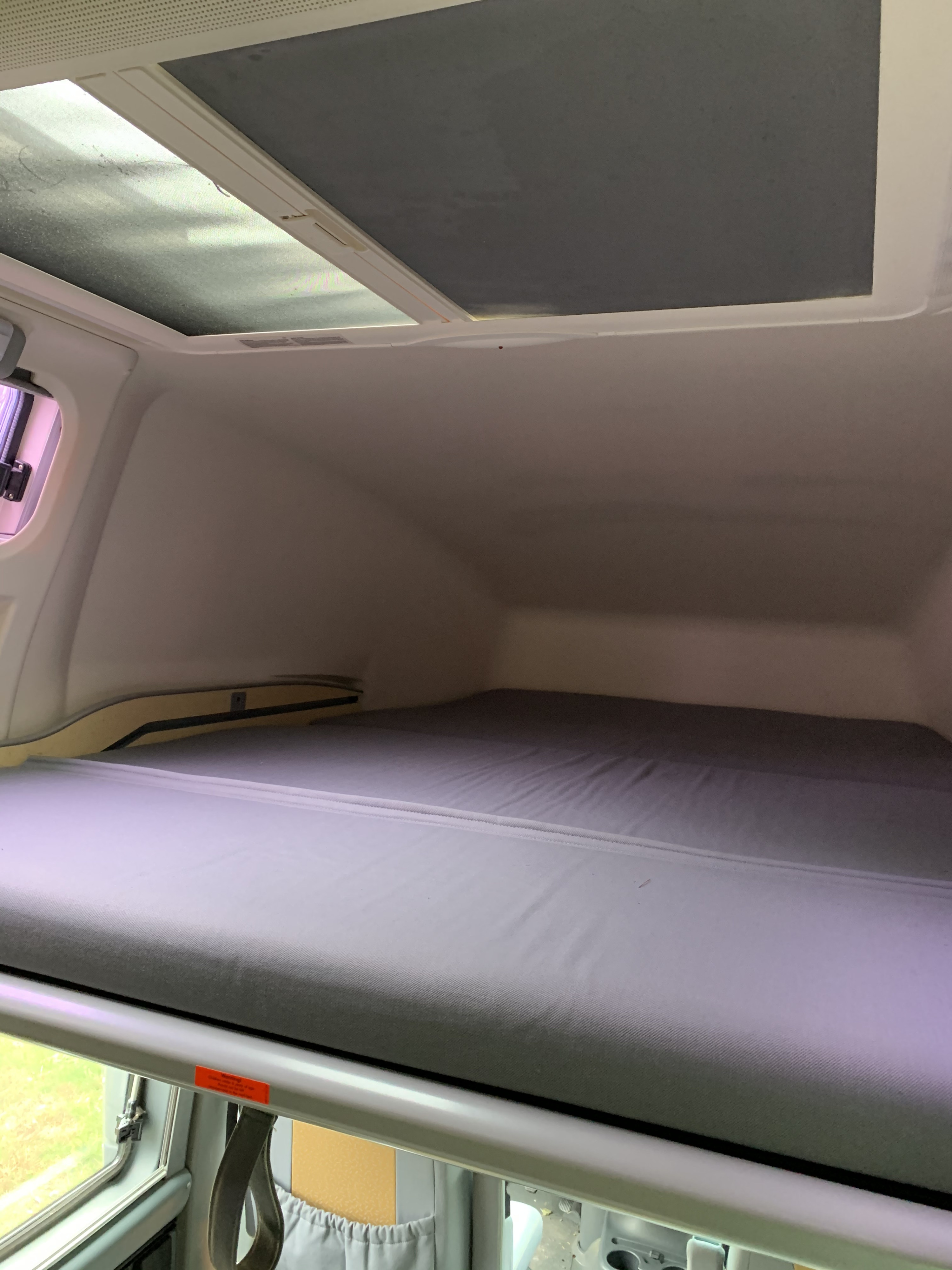 RV rental's cozy overhead bed with a grey mattress, dual skylights (one shaded), and a side window for camper trips.. Airstream Westfalia 2005