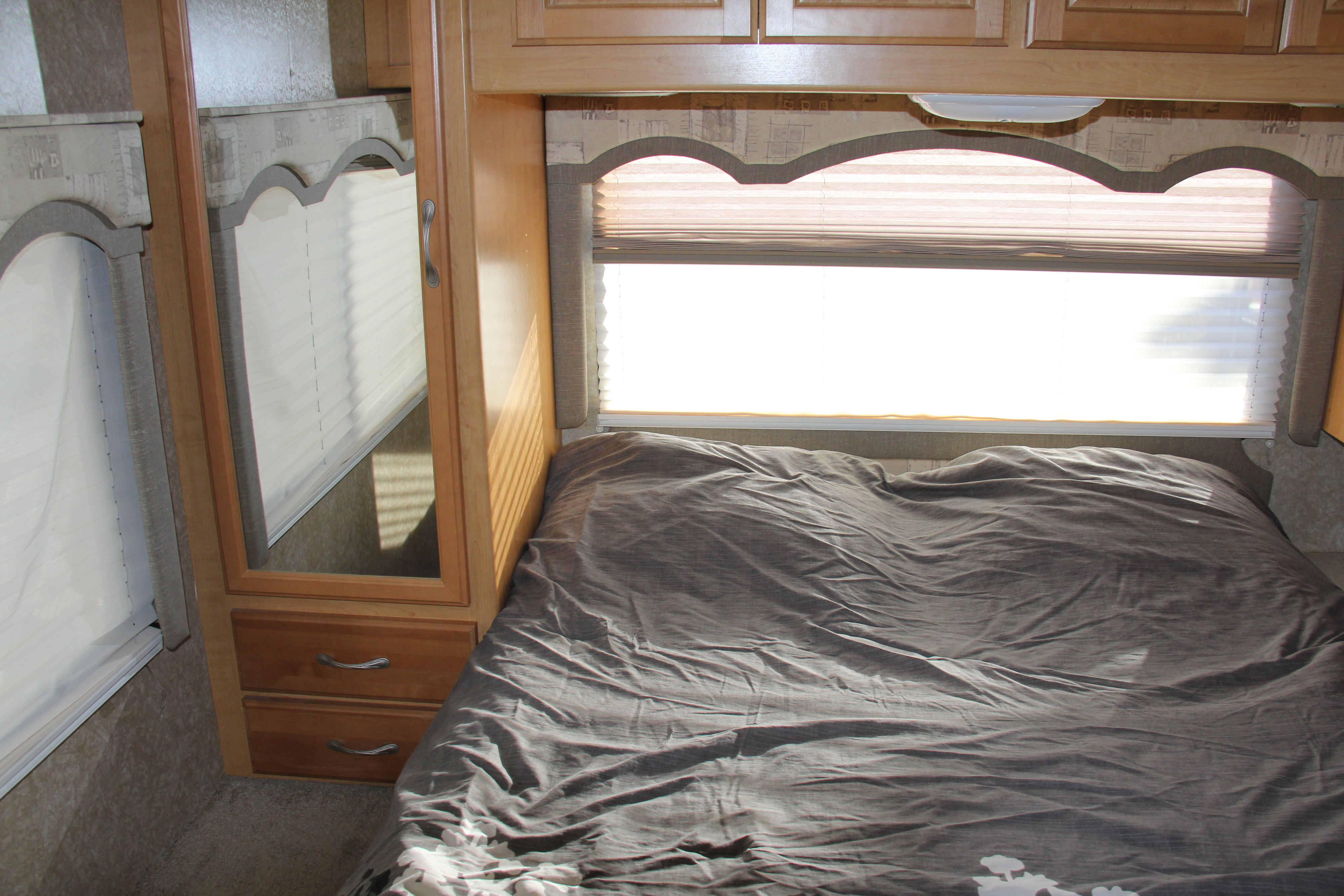 Bright RV rental bedroom featuring a comfortable bed, window with blinds, and built-in wood cabinets and mirrored wardrobe.. Thor Motor Coach Chateau 2007