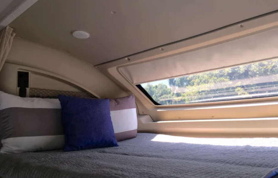 Comfortable bed with pillows and a window view of lush trees inside this cozy RV rental.. Entegra Coach Odyssey 25R 2019