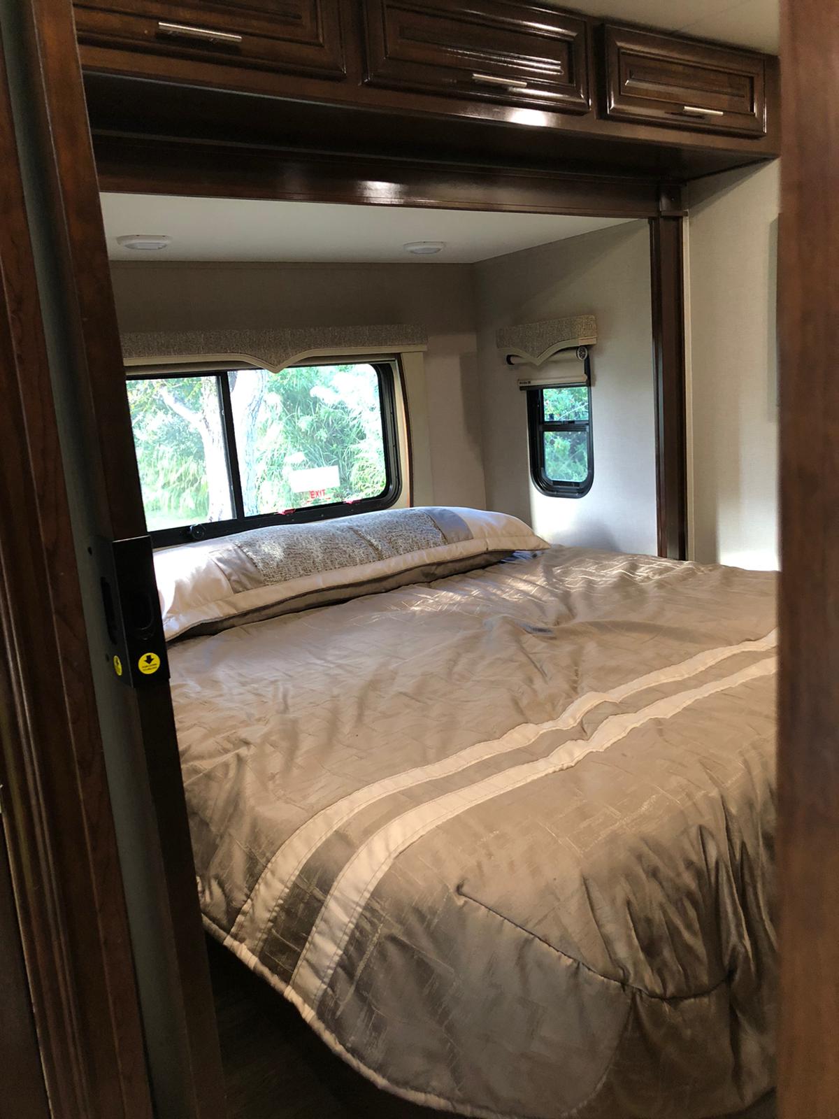 Spacious RV rental bedroom with a comfortable bed, bright windows, and overhead cabinets for your travels.. Forest River Georgetown 2018
