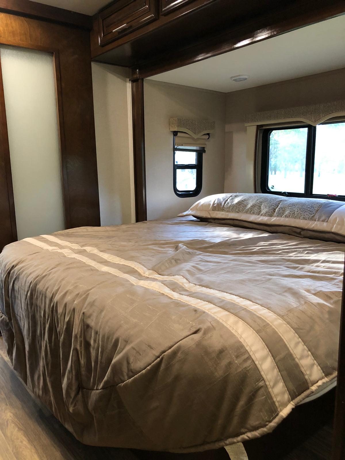 Comfortable RV rental bedroom: large bed with neutral bedding, wooden trim, and bright windows.. Forest River Georgetown 2018