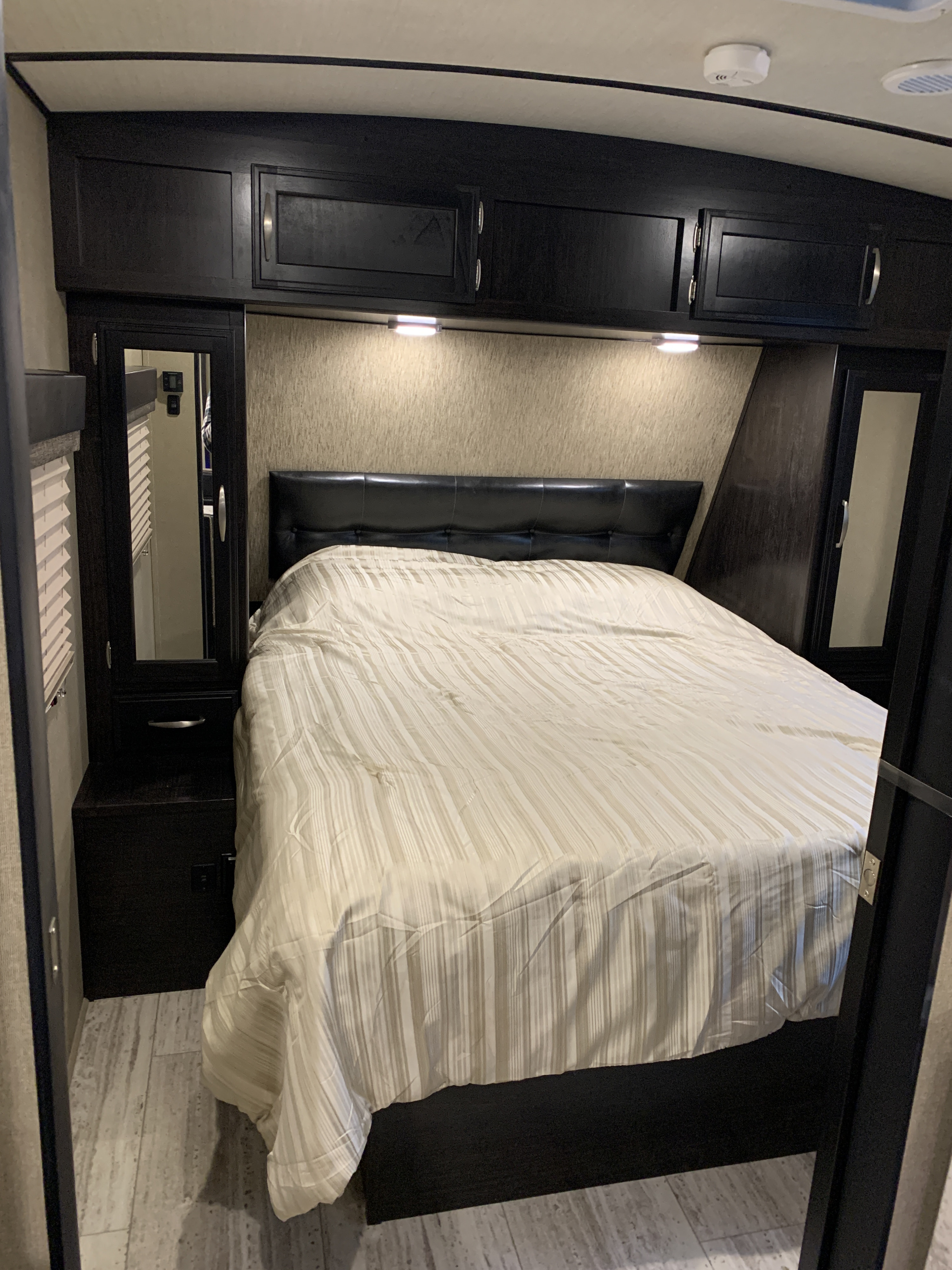 Cozy RV rental bedroom with dark wood cabinets, a comfy bed, and mirrored closets, perfect for your next trip.. Grand Design Imagine 2019