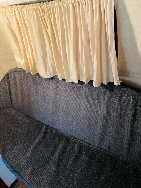 Cozy RV rental interior: dark blue sofa under cream valance curtains.. Scamp 16' 2018