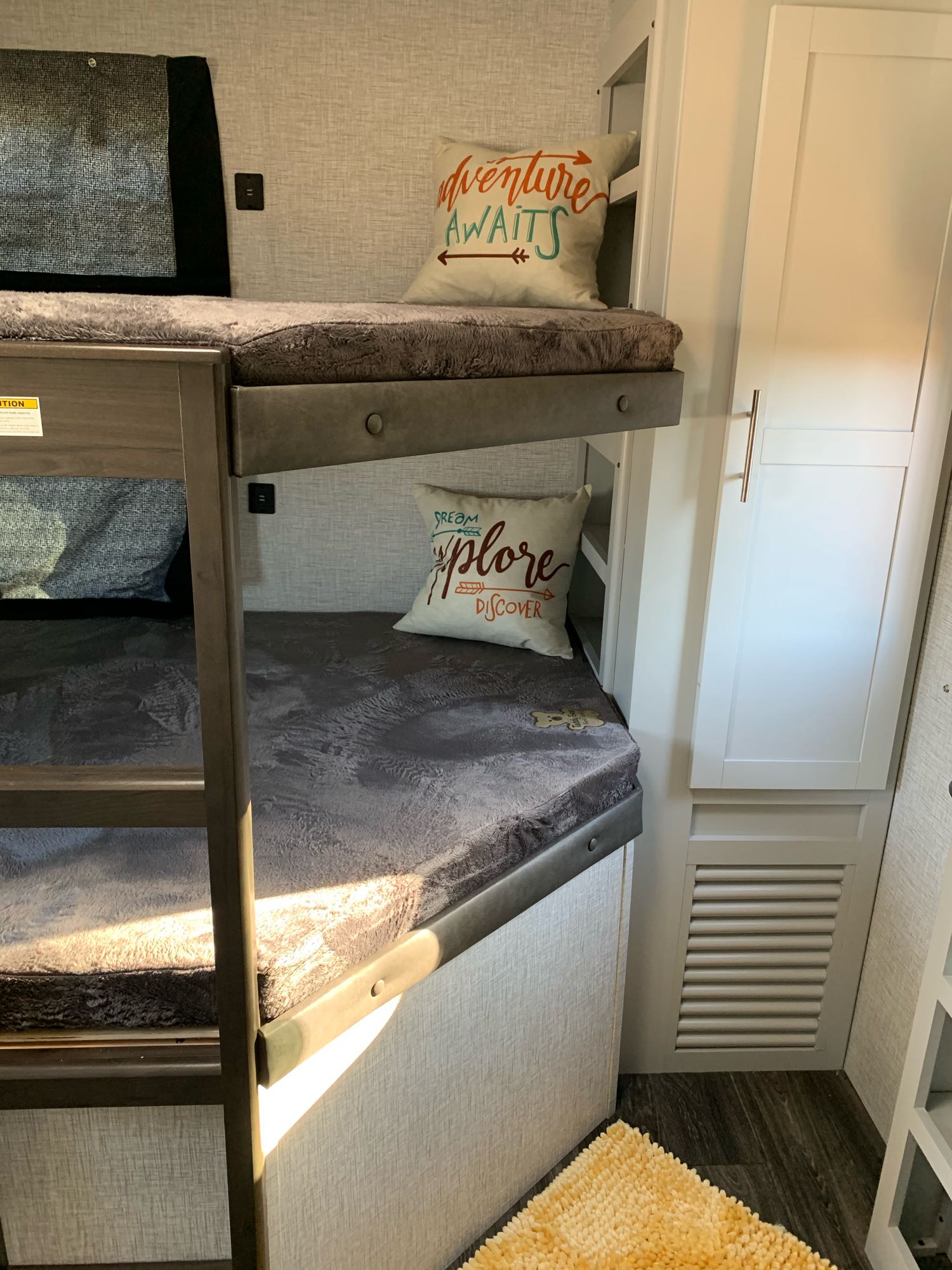 Cozy bunk beds in an RV rental, with soft gray bedding and adventure-themed pillows. A perfect sleeping area for your trip!. Keystone RV Bullet Ultra Lite 2021