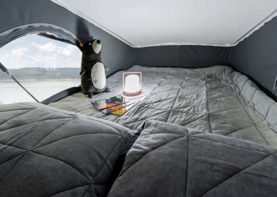 Cozy RV rental pop-top sleeping area with a quilted bed, soft lighting, and a scenic river view outside.. Winnebago Winnebago 2022