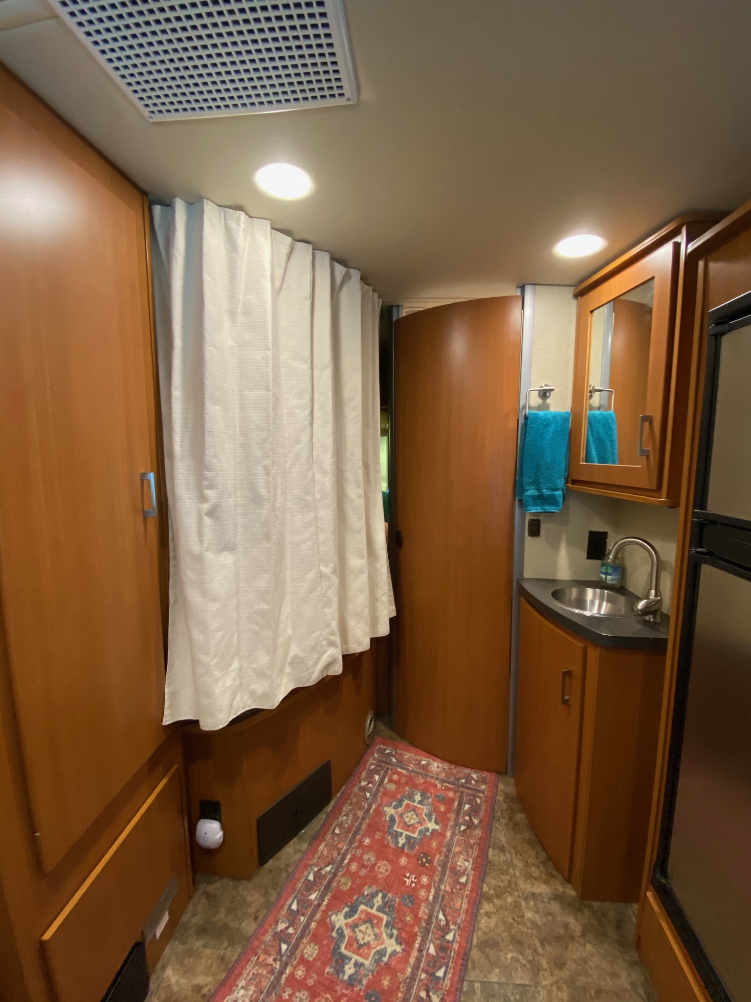 Compact RV rental bathroom with sink, mirror, and shower curtain. Wooden cabinets offer storage in this functional mobile space.. Winnebago View 2014