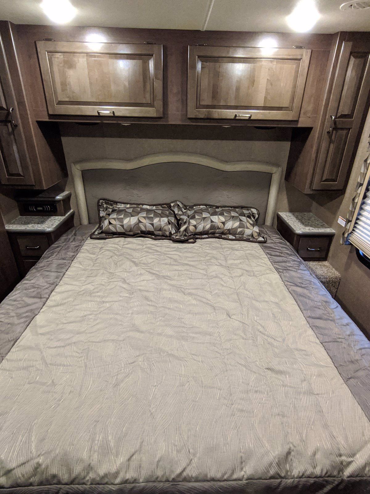 Comfortable RV rental bedroom with a large bed, patterned bedding, overhead cabinets, and built-in nightstands.. Other Hurricane 2017