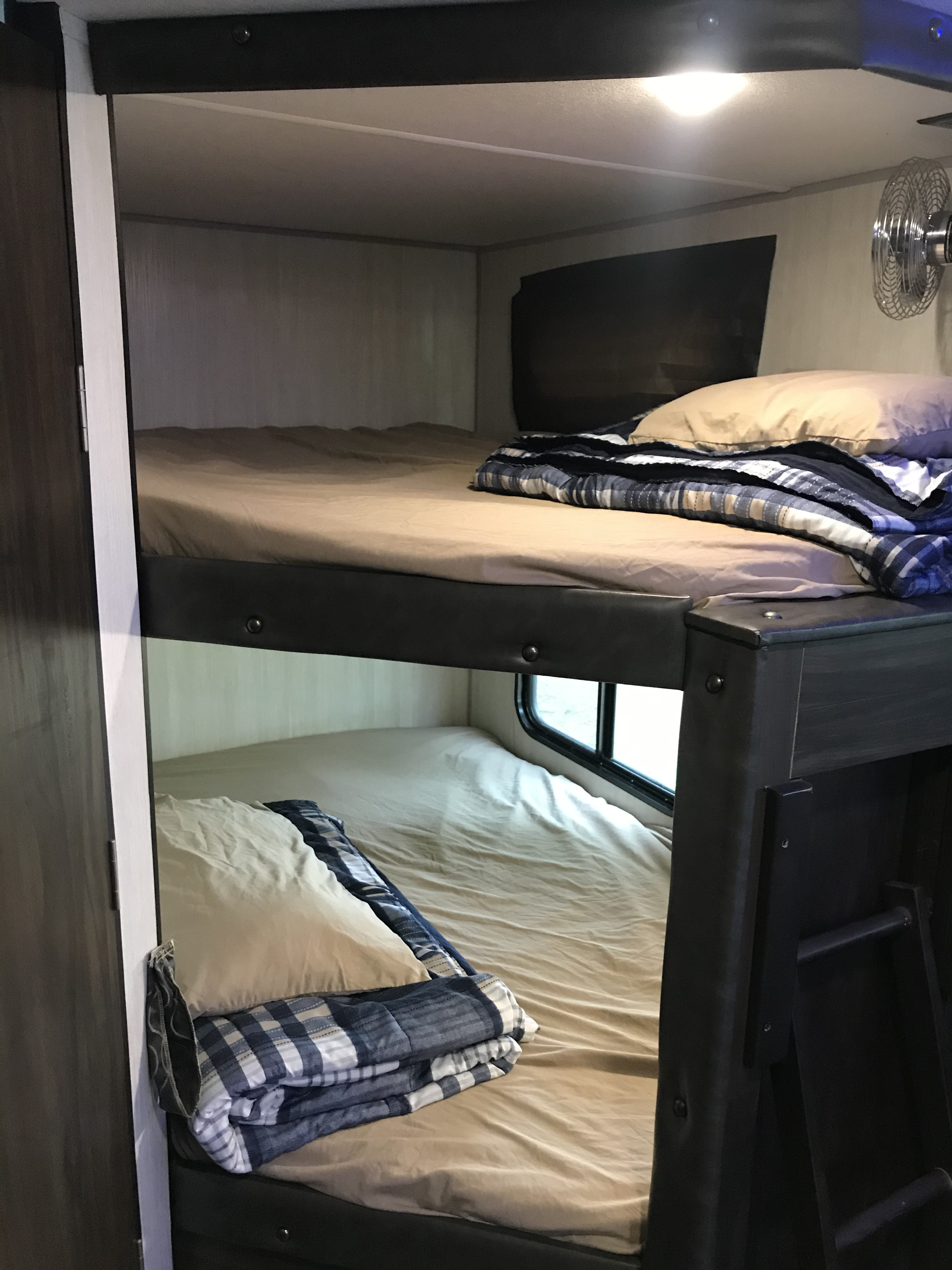This RV rental features cozy bunk beds, complete with tan sheets and plaid blankets, and a fan on the top bunk.. Forest River Grey Wolf 26DBH 2020