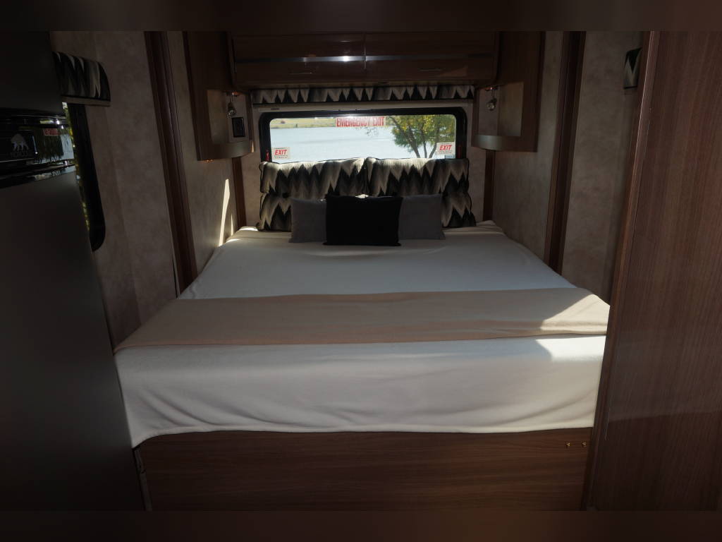 Cozy RV rental bedroom featuring a comfortable bed, patterned pillows, a window with a view, and warm wood interior.. Winnebago View 2015