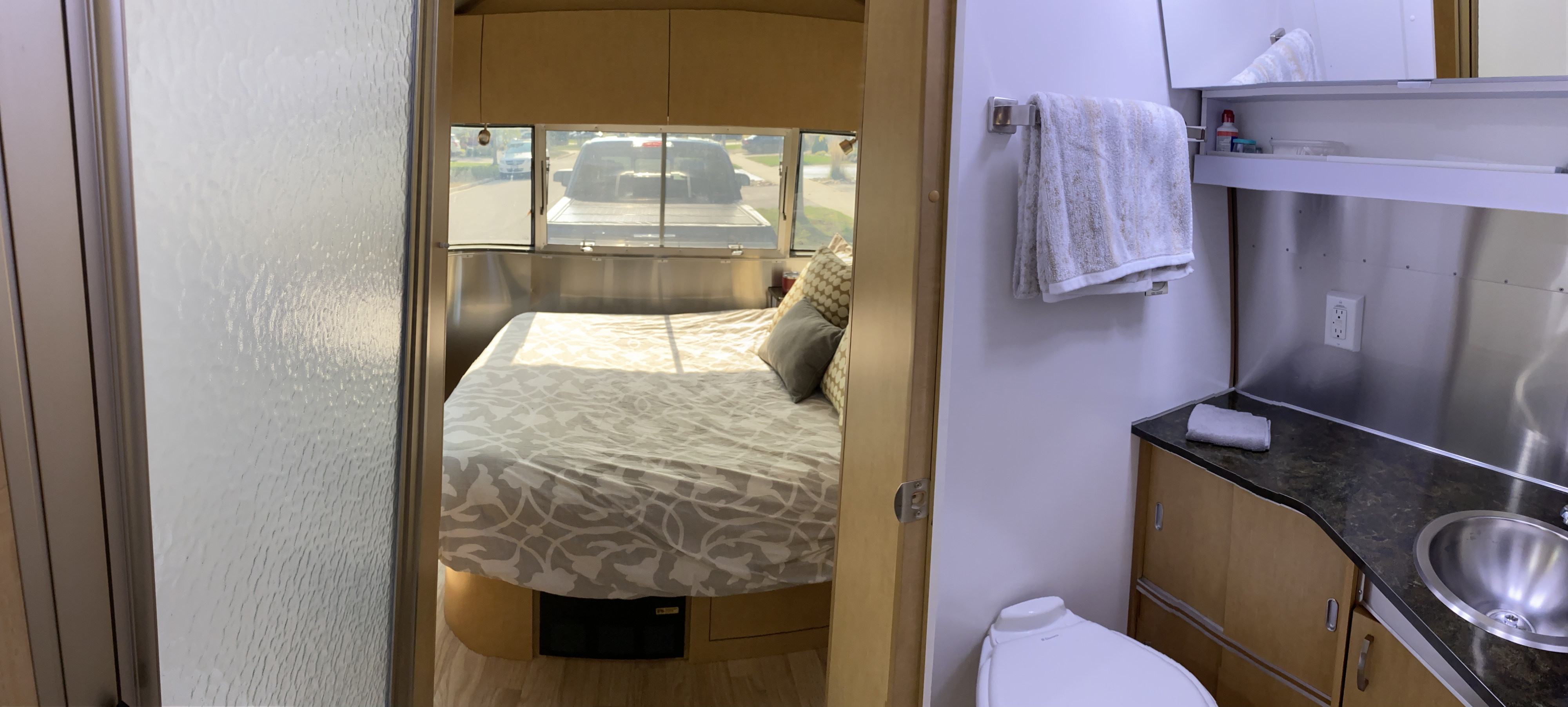 RV rental interior: cozy bedroom with a patterned bed visible from the compact bathroom, featuring a toilet, sink, and shower.. Airstream Flying Cloud 2016