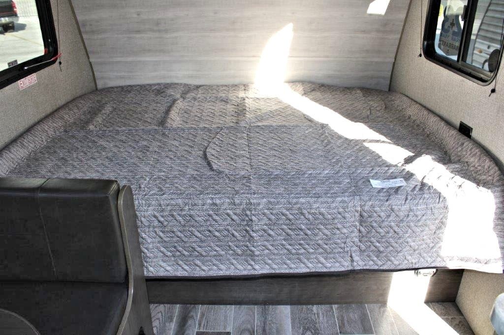RV rental's cozy gray quilted bed, possibly a dinette conversion, with modern wood accents & bright sunlight.. Jayco Jay Flight 2021