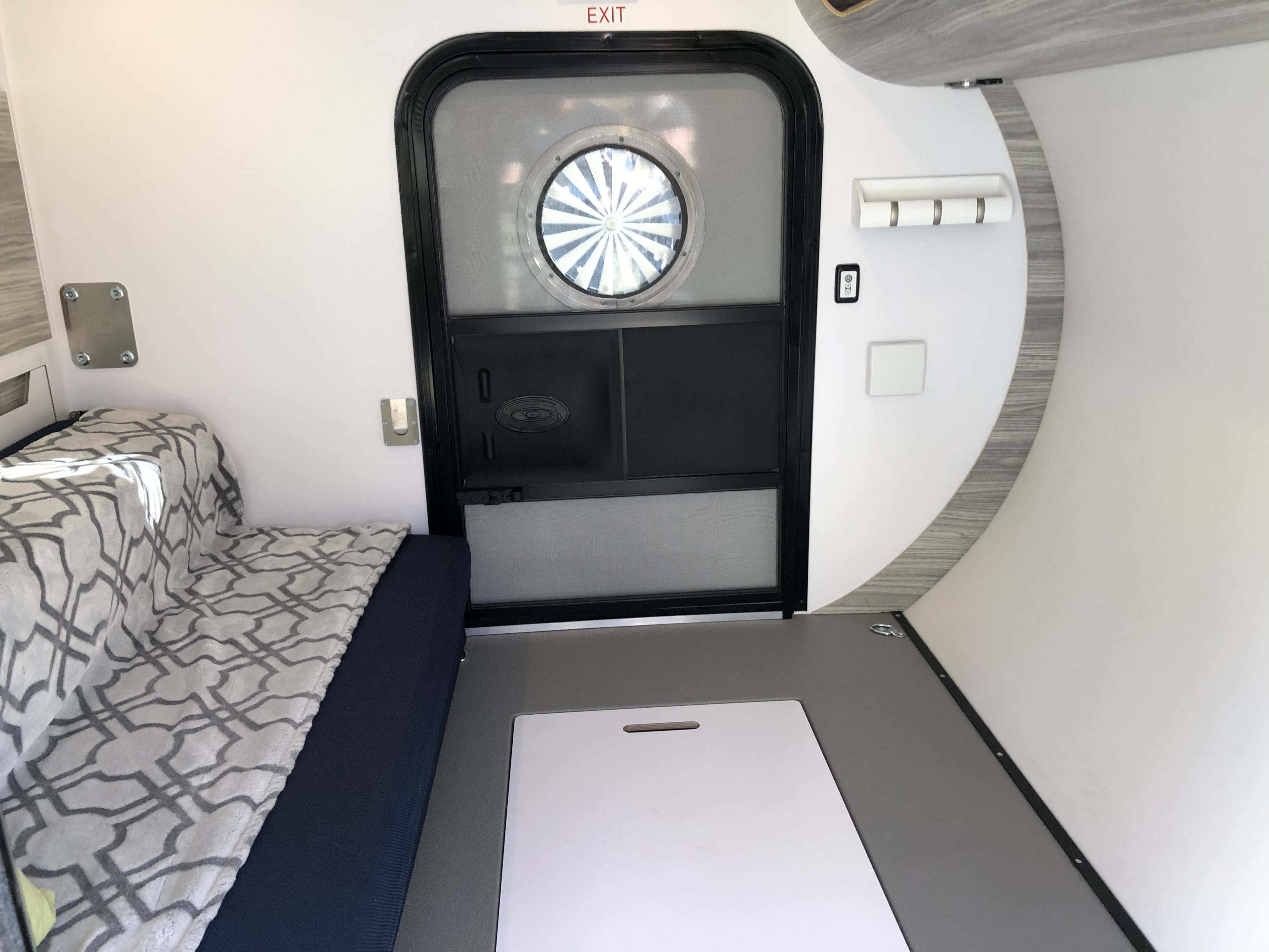 Experience RV rental comfort: interior shows bed, door with porthole, and floor panel in a compact camper.. Bean Trailer Mean 2020
