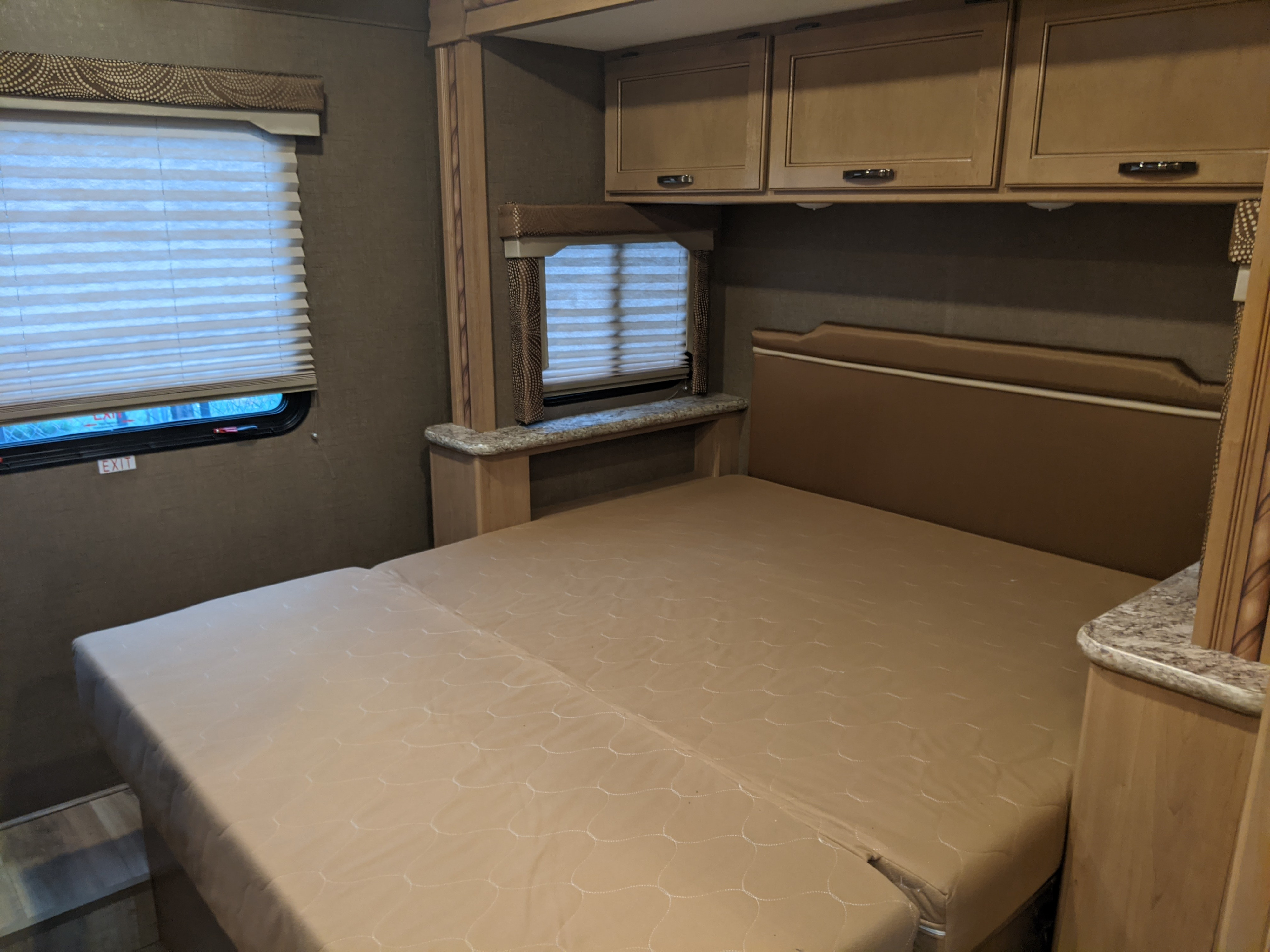 View of an RV rental bedroom featuring a tan convertible bed, overhead cabinets, and an emergency exit window.. Thor Motor Coach Freedom Elite 2018