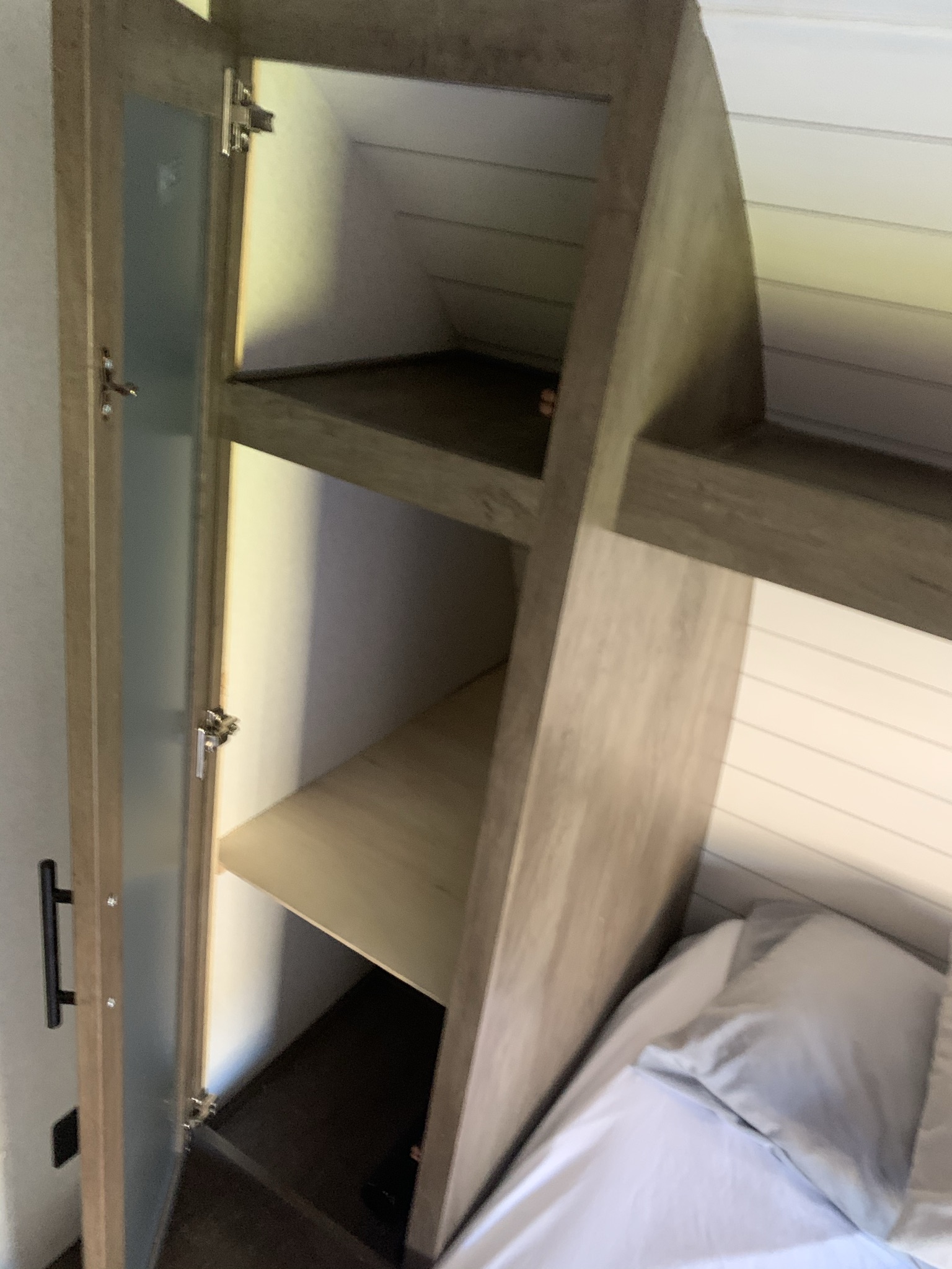 An RV rental interior showing a compact bedroom with a cozy bed and light-wood storage, including shelves and a cabinet.. Forest River Salem Cruise Lite 2020