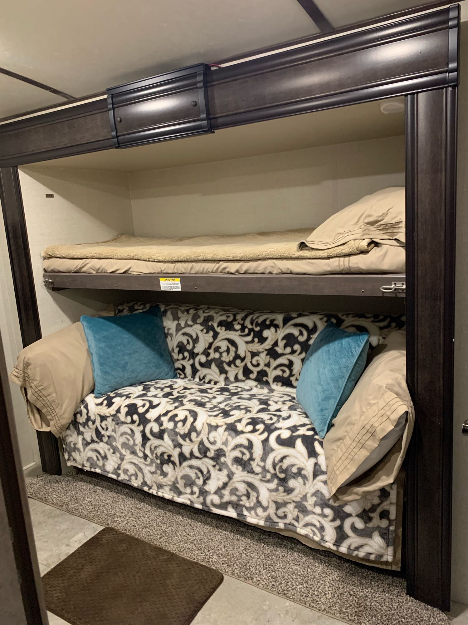 Cozy RV rental bunk area: an upper bed with bedding and a lower sofa bed with patterned blanket.. Crossroads Sunset Trail 2018