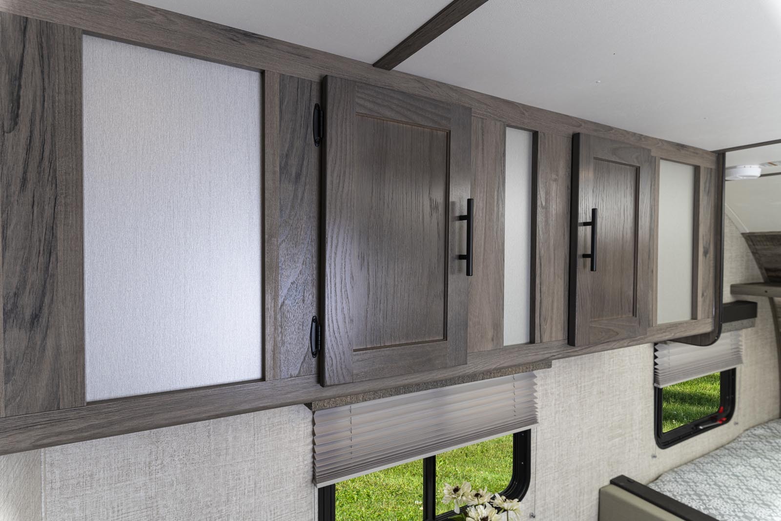 RV rental bedroom interior featuring modern woodgrain overhead cabinets, windows, and blinds.. Gulf Stream Amerilite 2021