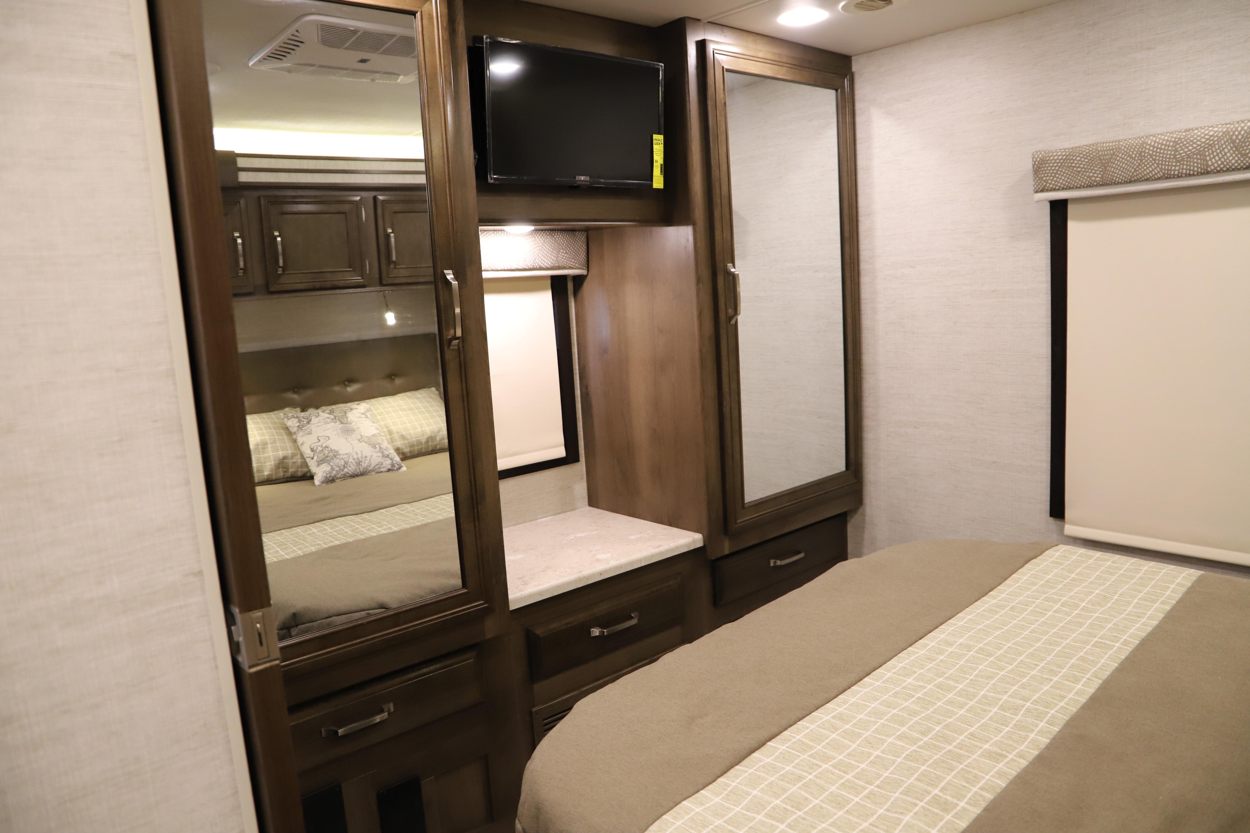 View of a modern RV rental bedroom showing a bed, built-in mirrored cabinets, and a flat-screen TV.. Entegra Coach Other 2021