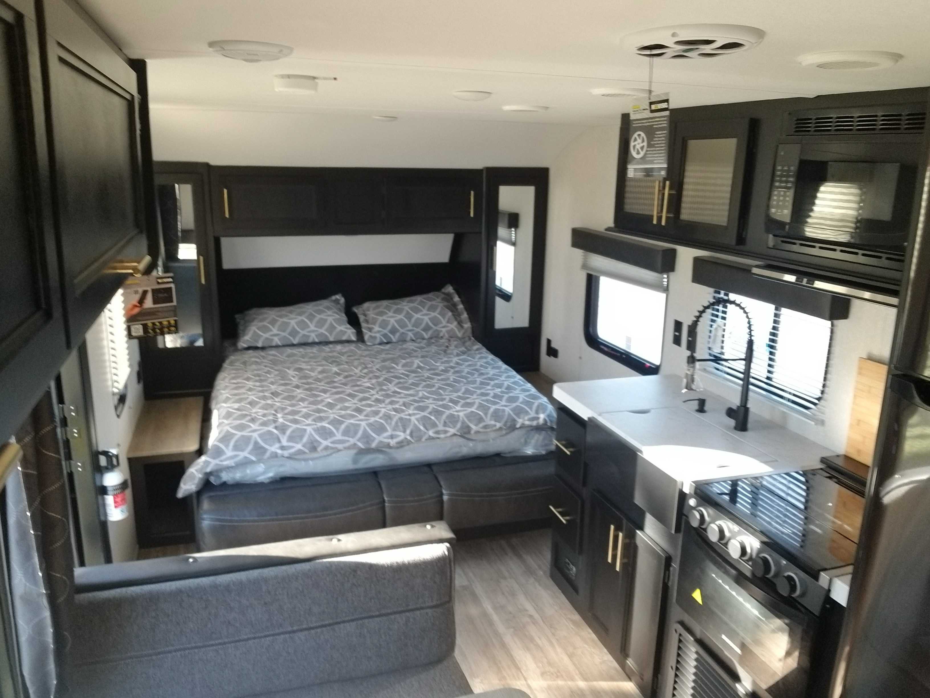 Spacious RV rental interior featuring a cozy bedroom area with a bed, and a well-equipped kitchen with stove, sink, and microwave.. Forest River Cherokee Grey Wolf 2021