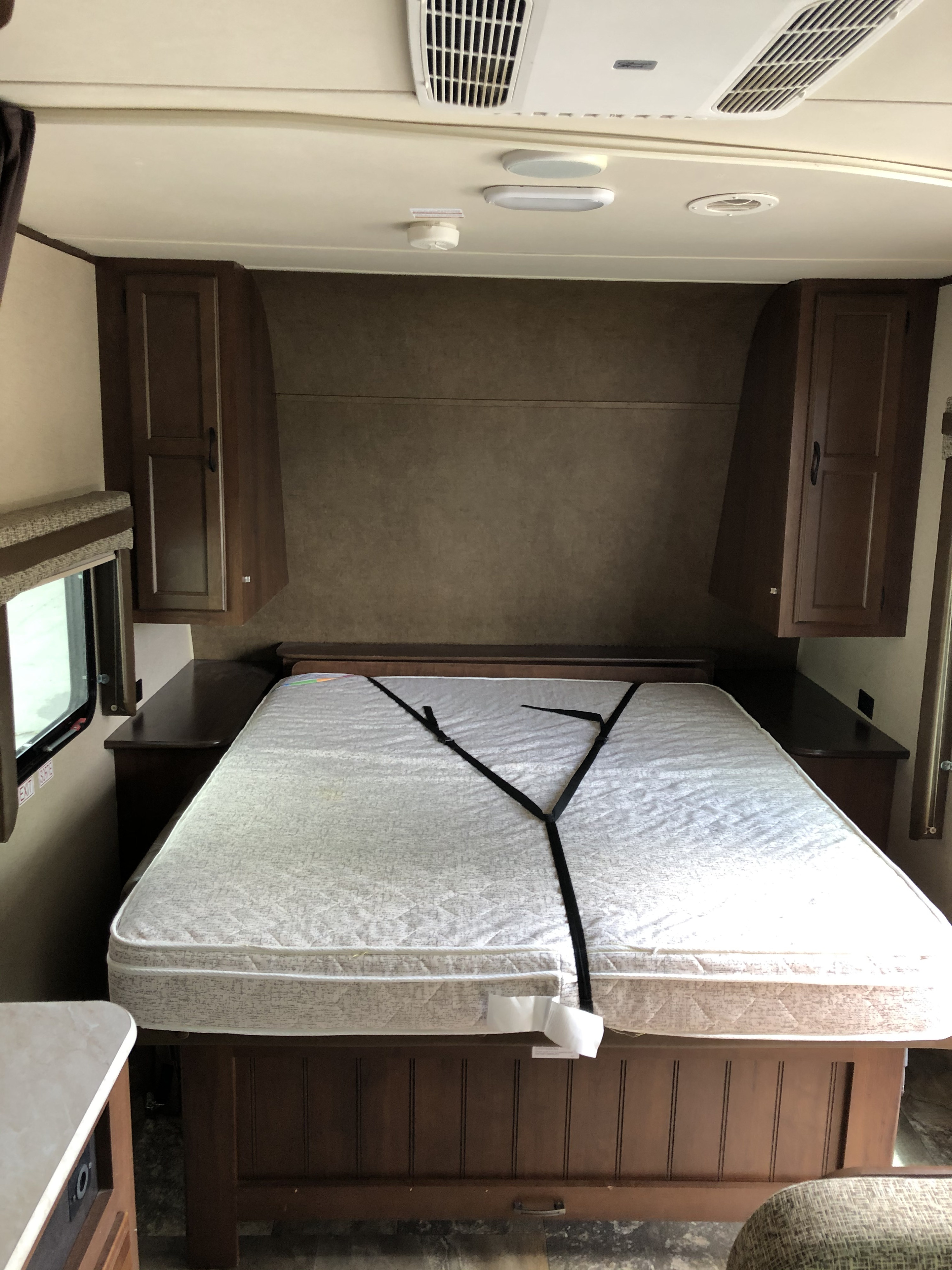 Inside an RV rental, this clean bedroom features a secured mattress on a platform bed, side tables, and overhead cabinets.. Jayco Jay Flight 2015
