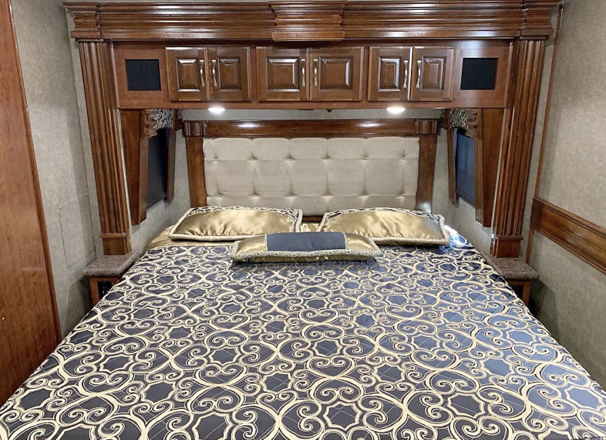 Luxury RV rental bedroom featuring a large bed, tufted headboard, and extensive dark wood cabinetry.. Fleetwood Discovery 2019